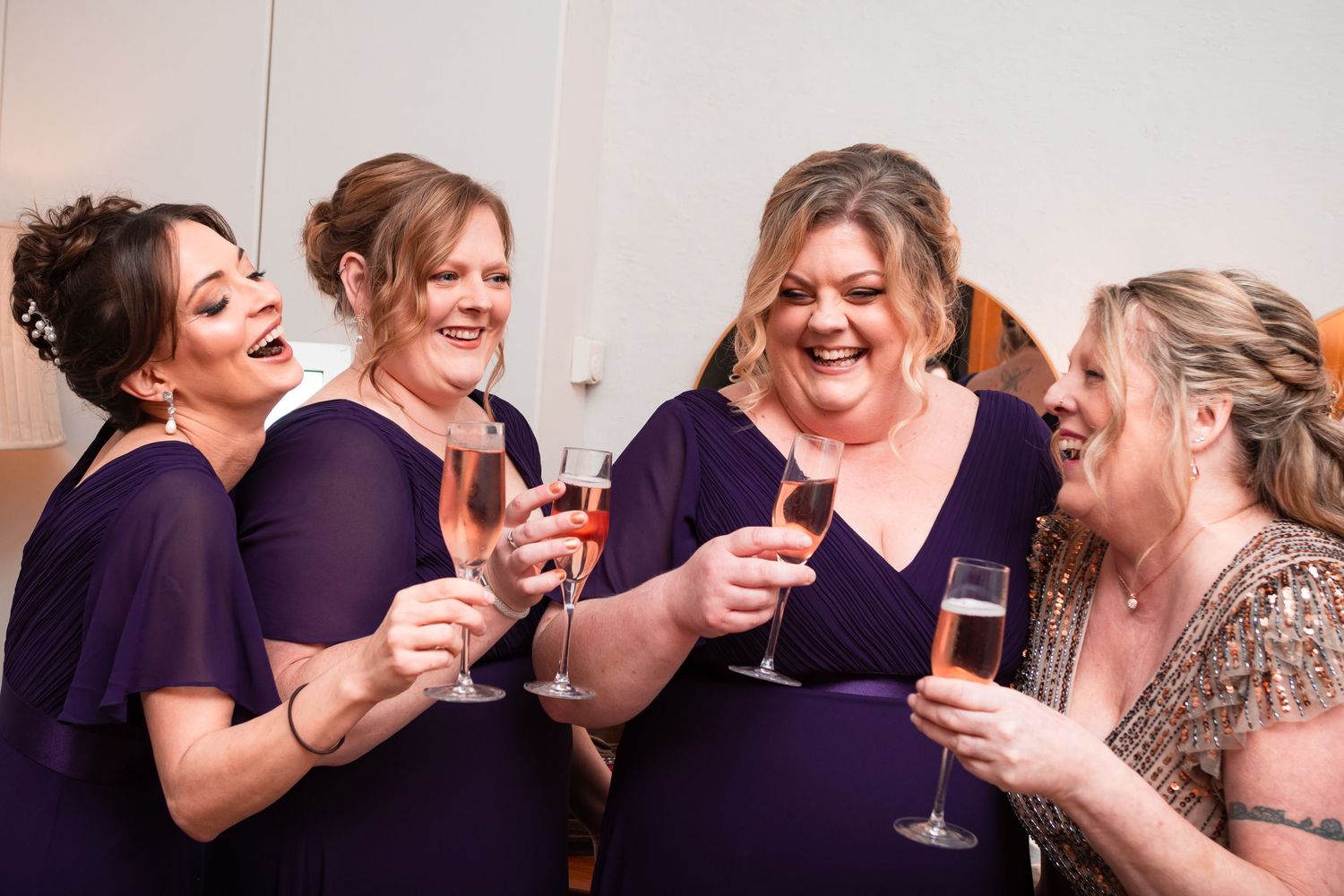 People in purple bridesmaid dresses share laughter and wine glasses during a celebratory moment.
