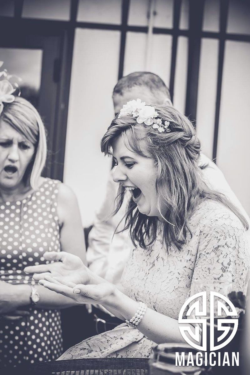 A candid black and white photo shows a bride and guest reacting with excited expressions during a wedding event.