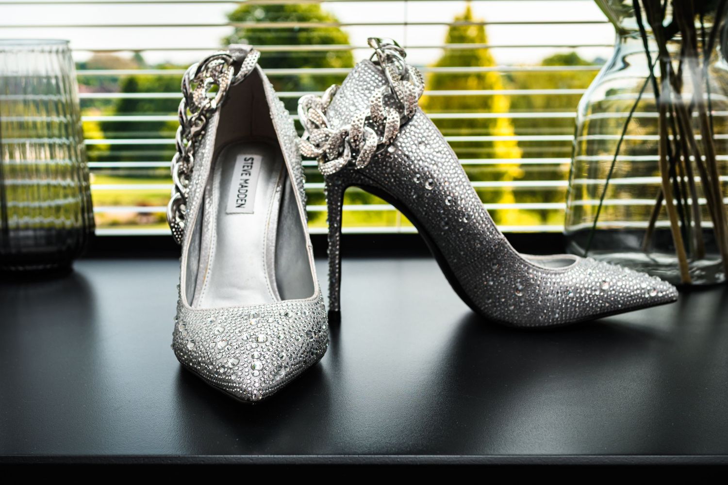Sparkly silver designer high heels displayed on a dark surface with natural lighting.