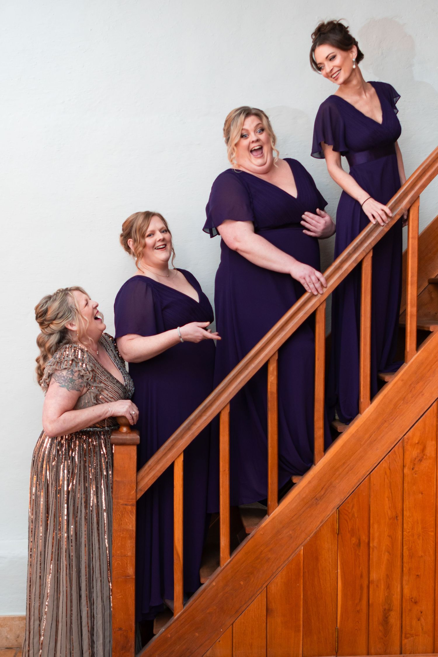 Wedding party in purple dresses and a sparkly gold gown pose together along wooden staircase.