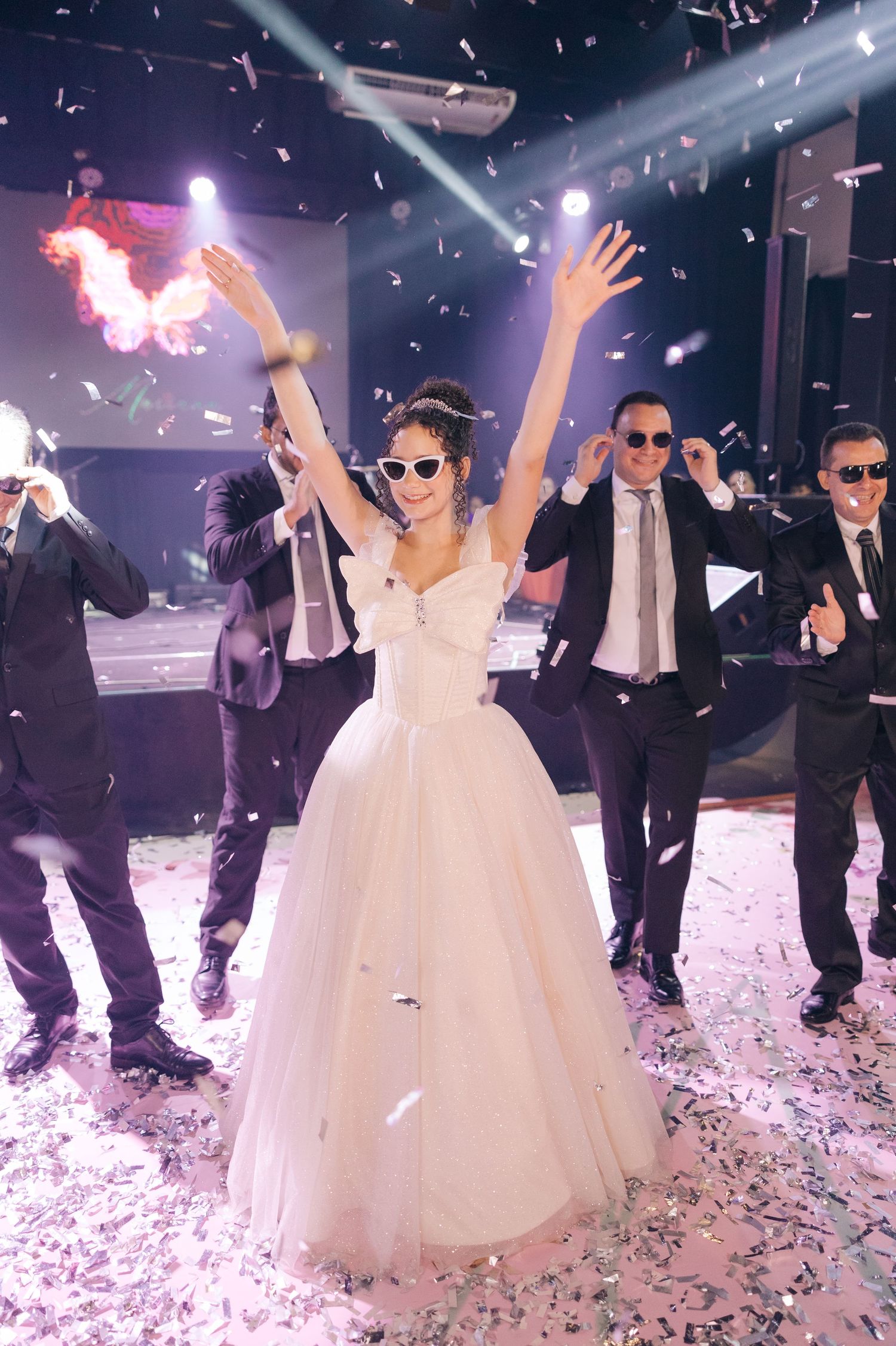 Wedding celebration with confetti and white ballgown amidst dramatic stage lighting.