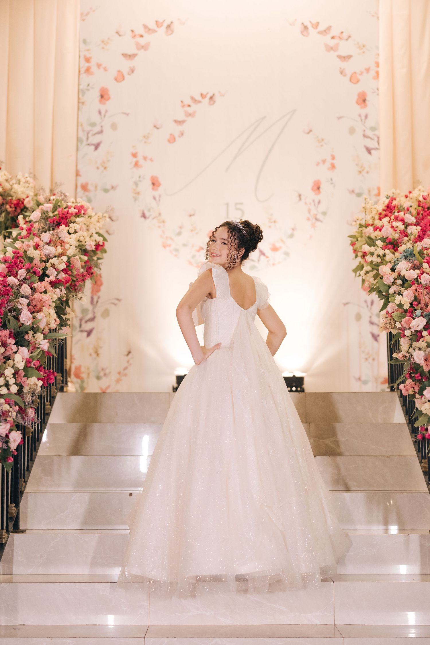 Elegant white wedding gown showcased against romantic floral arch backdrop and marble steps.