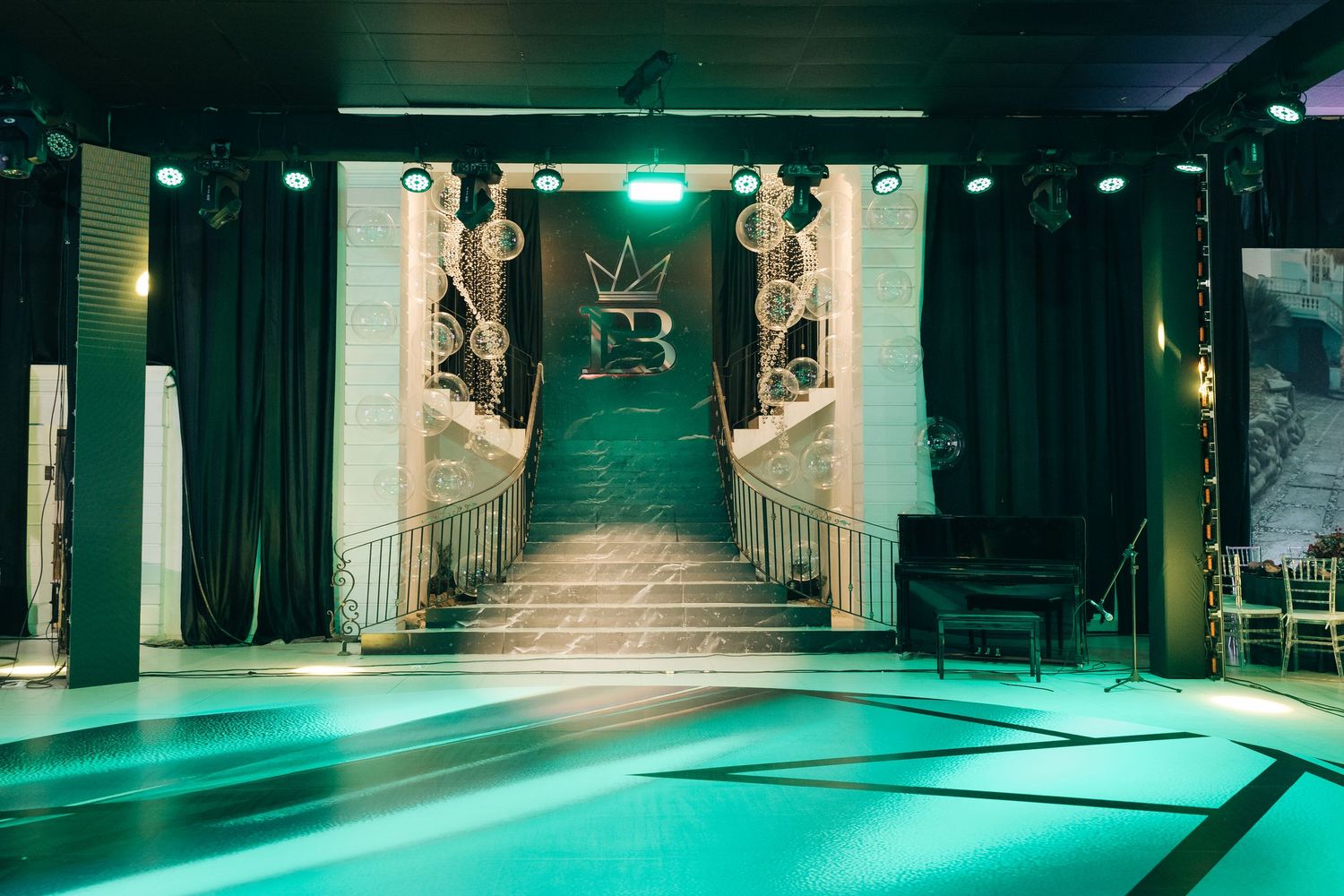 A modern nightclub space with emerald green lighting and white columns featuring a raised stage platform and velvet curtains.