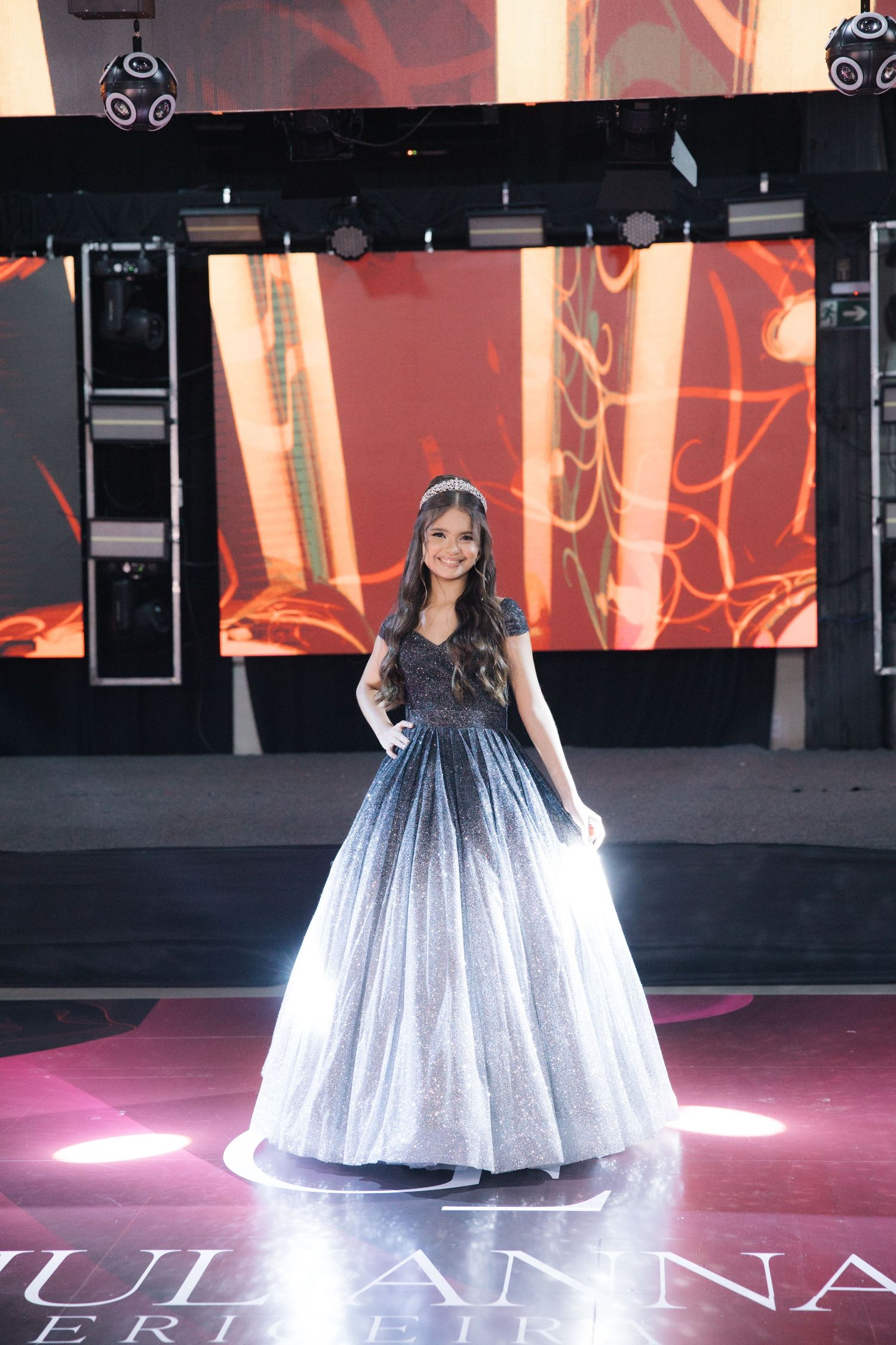 A sparkling ball gown on stage with dramatic lighting and digital backdrop.