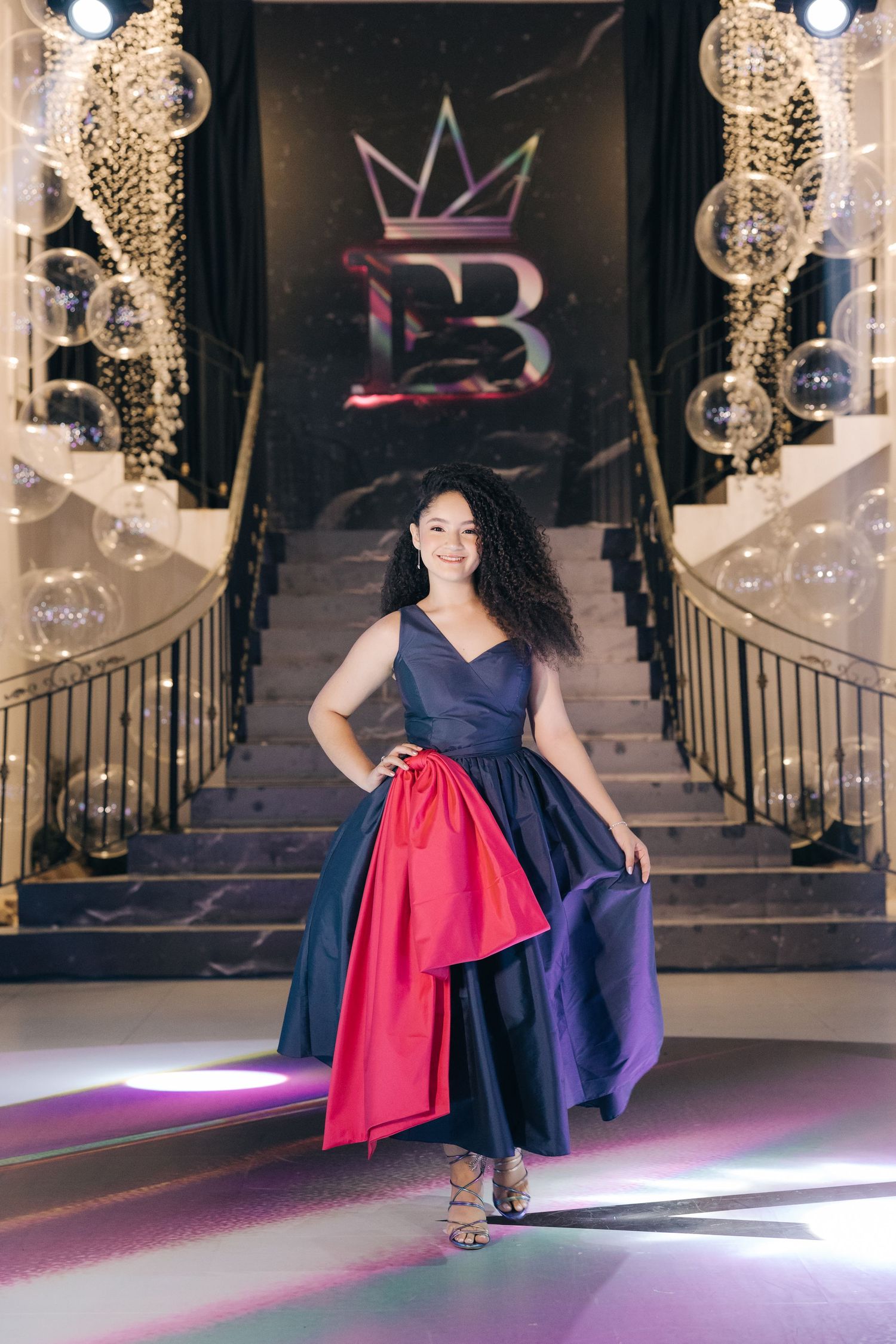 An elegant navy gown with red accent panel photographed on a grand staircase with crystal chandeliers.
