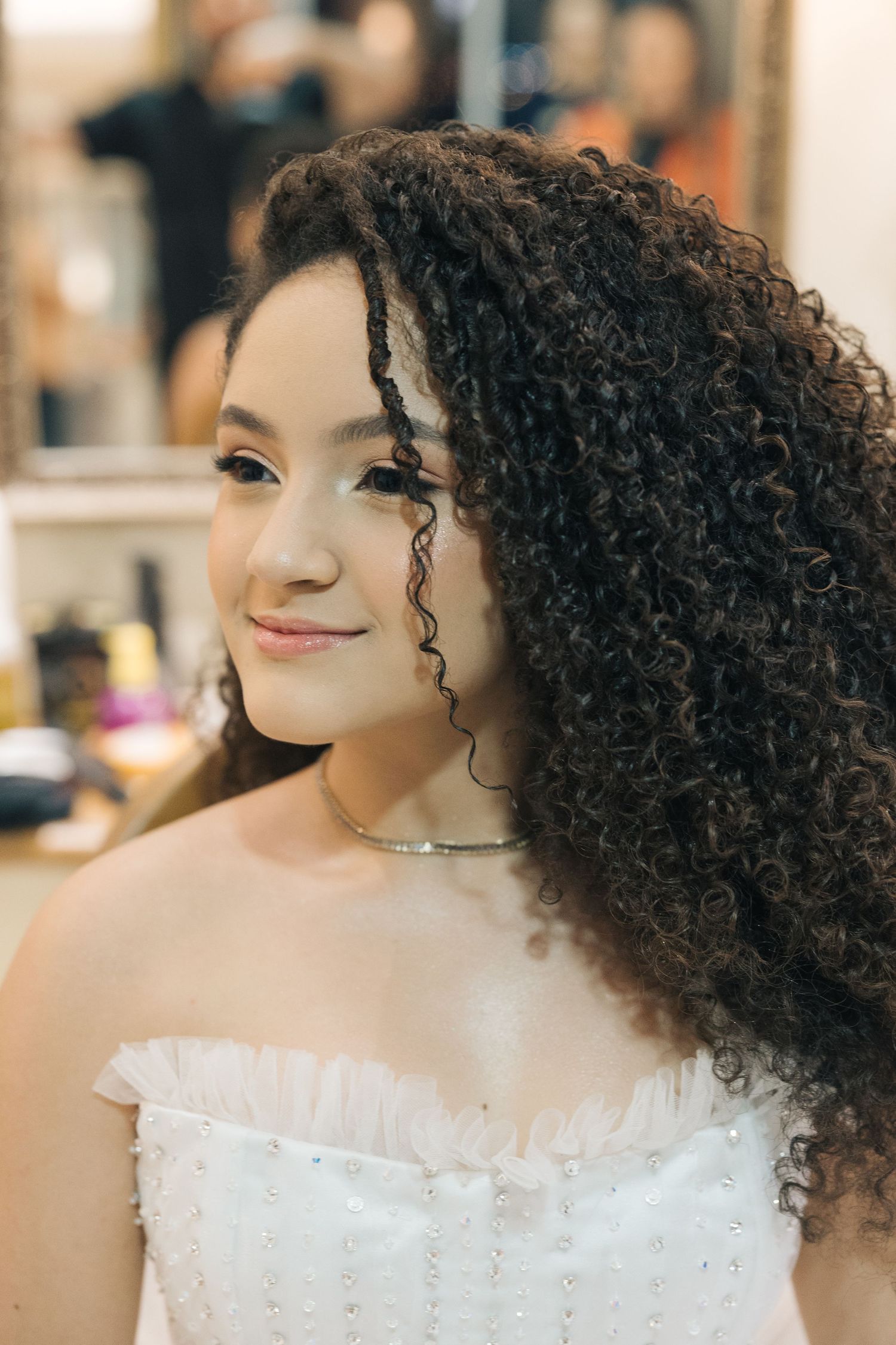 A beautiful white strapless dress with intricate details and flowing curly hair styled for a special occasion.