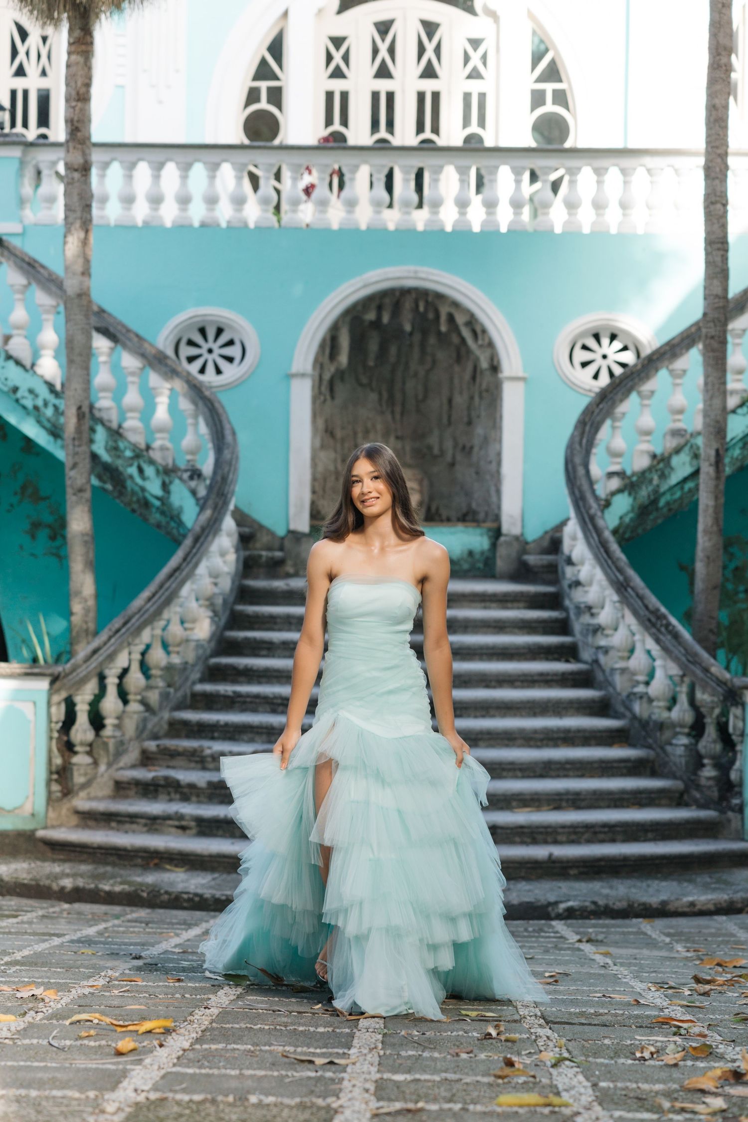 Stunning seafoam green gown photographed in front of a turquoise colonial staircase with ornate white railings.