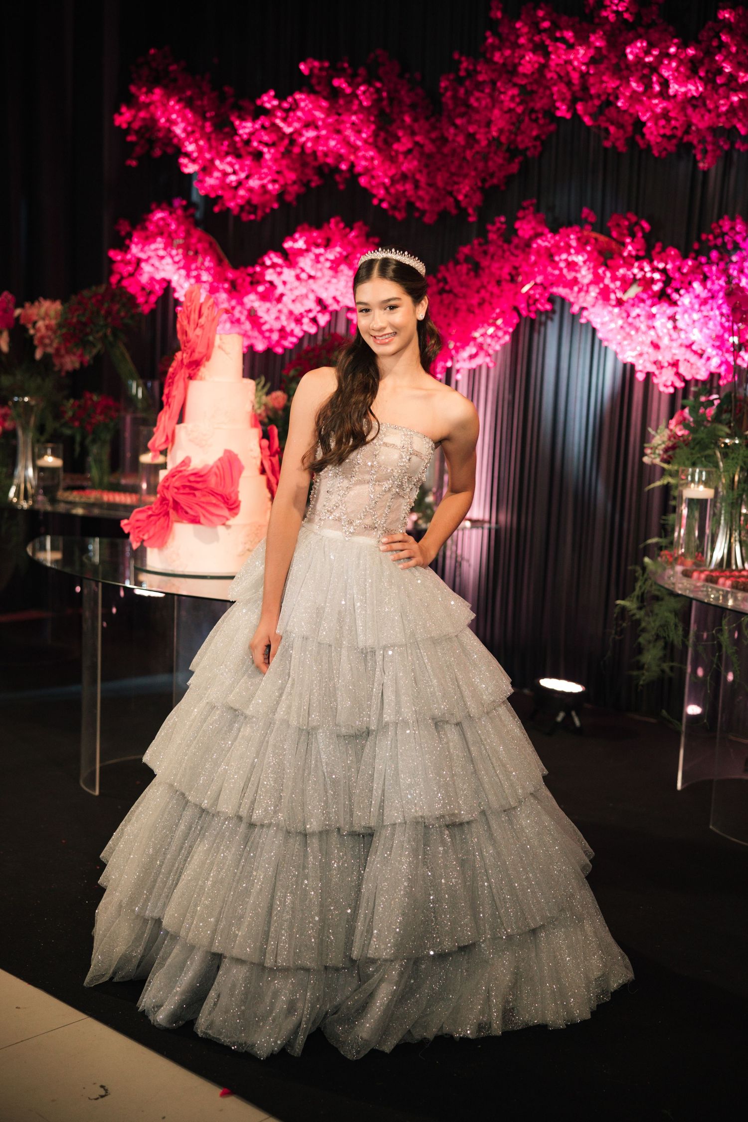 An elegant strapless ballgown with layered tulle skirt shown against a backdrop of fuchsia floral decorations.