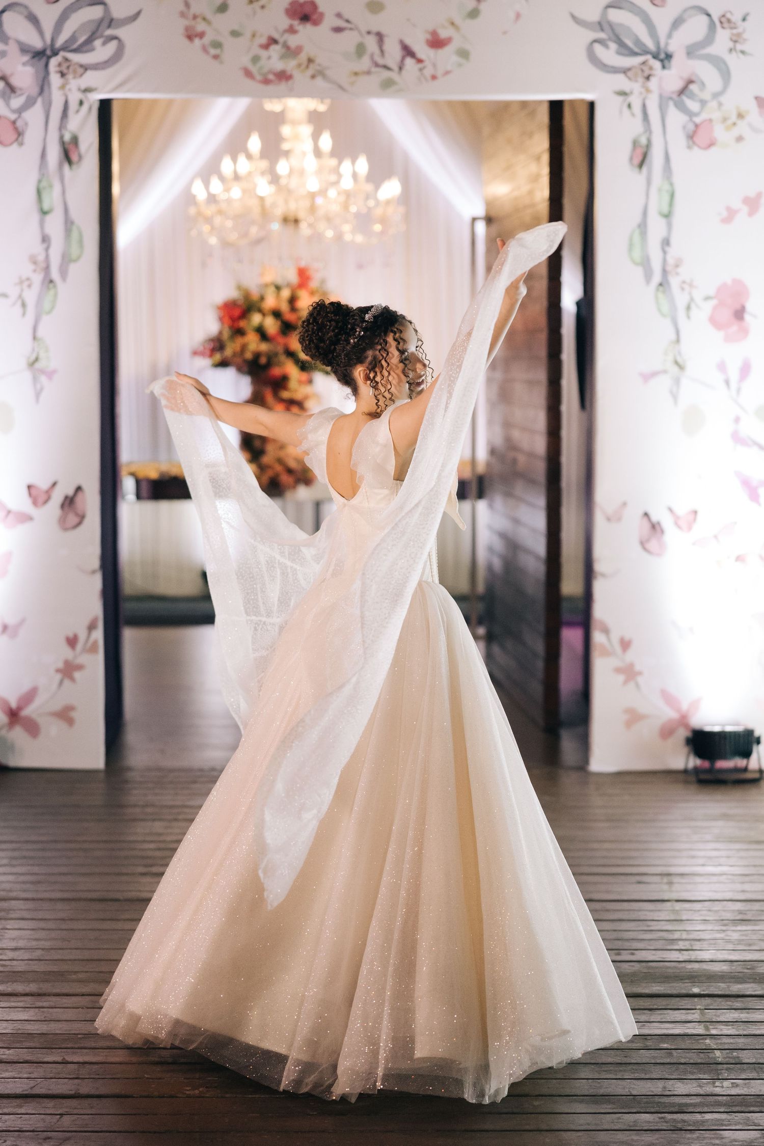 Ethereal bridal portrait with flowing tulle dress in elegant venue with chandelier.