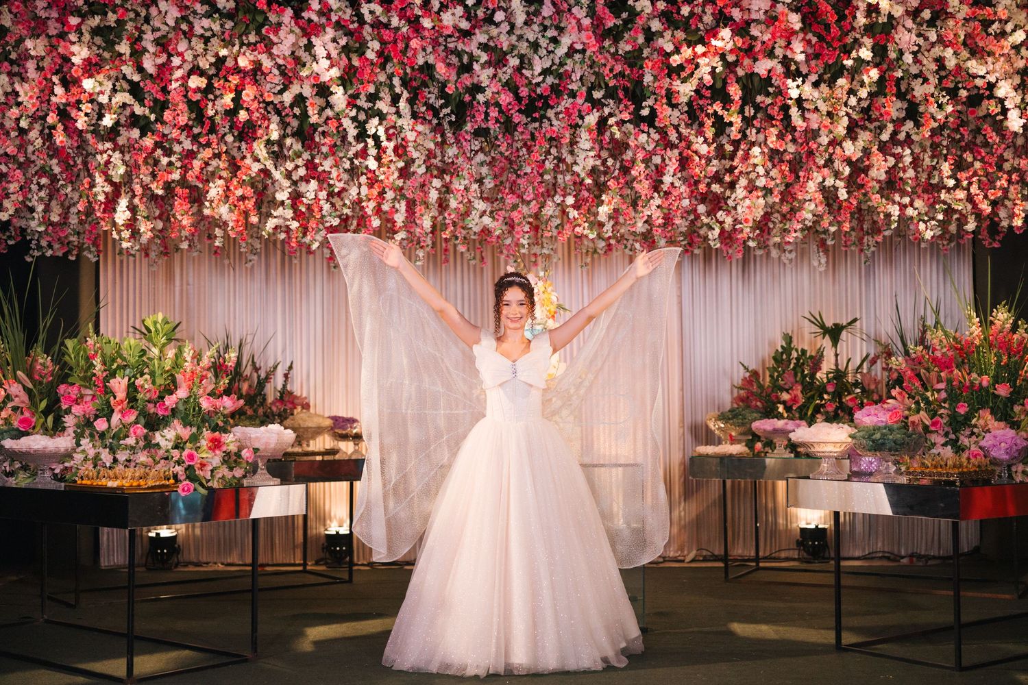 A stunning wedding reception setup with cascading pink floral ceiling installation above elegant buffet tables and white drapery.