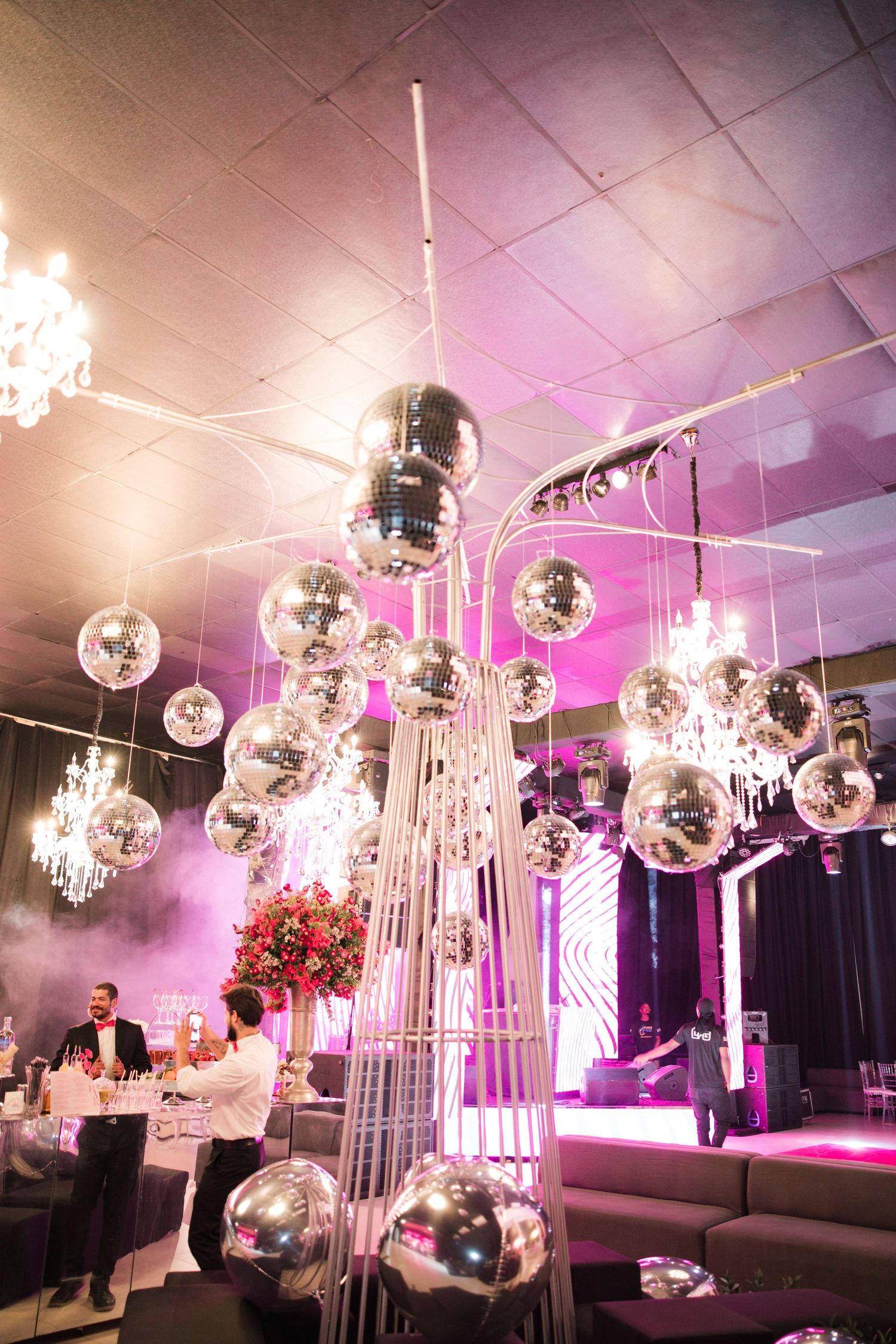 Glamorous event space decorated with hanging disco balls, crystal chandeliers and pink mood lighting.