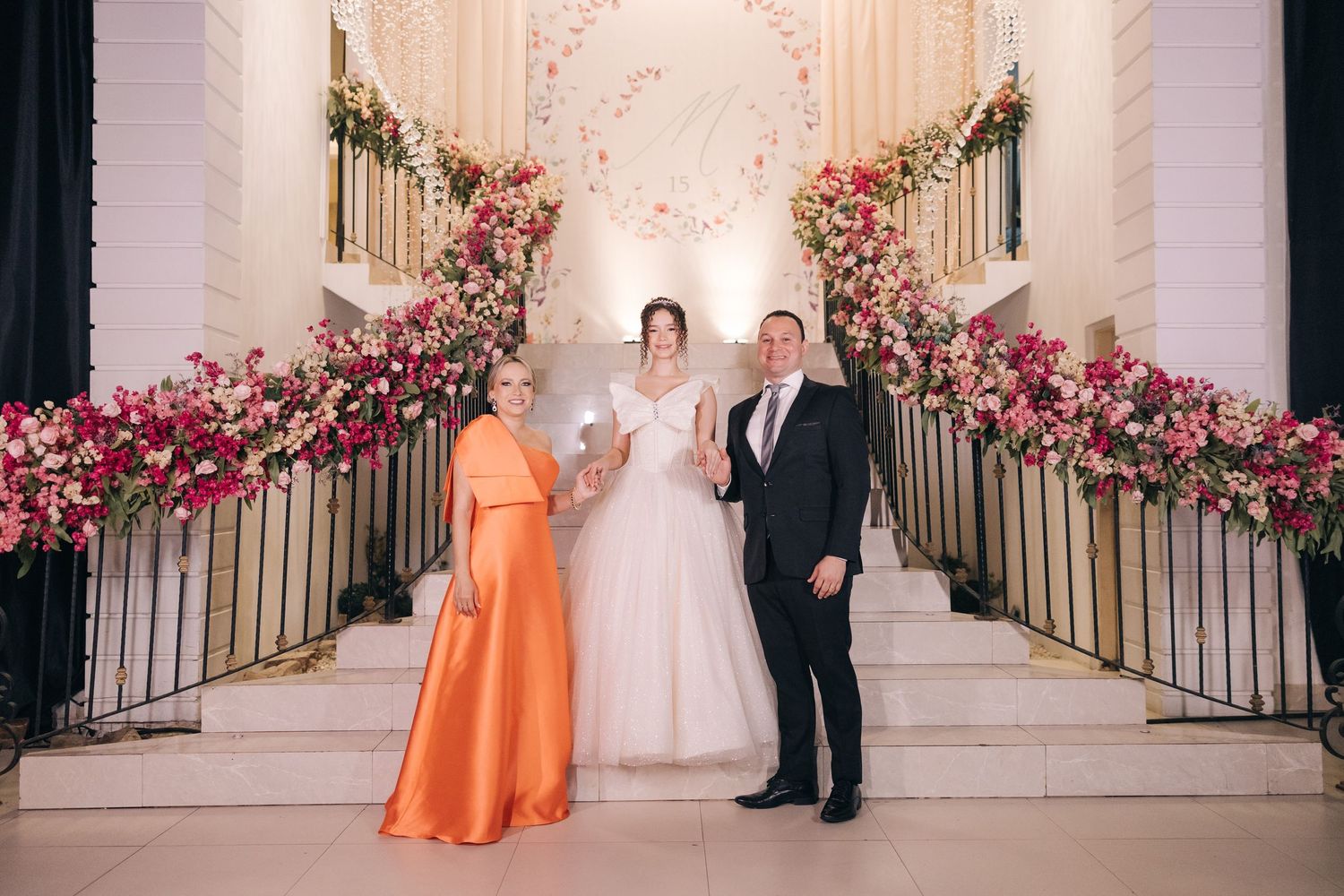 Wedding ceremony at elegant venue with ornate staircase decorated with pink and coral floral arrangements.