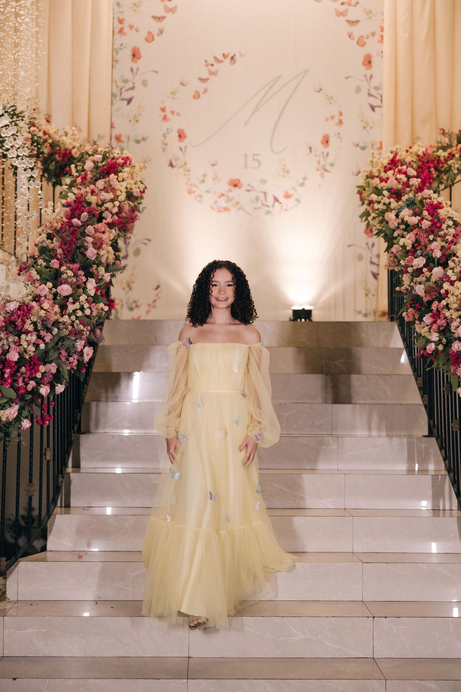 Ethereal yellow off-shoulder gown worn on grand staircase decorated with pink and coral floral arrangements.