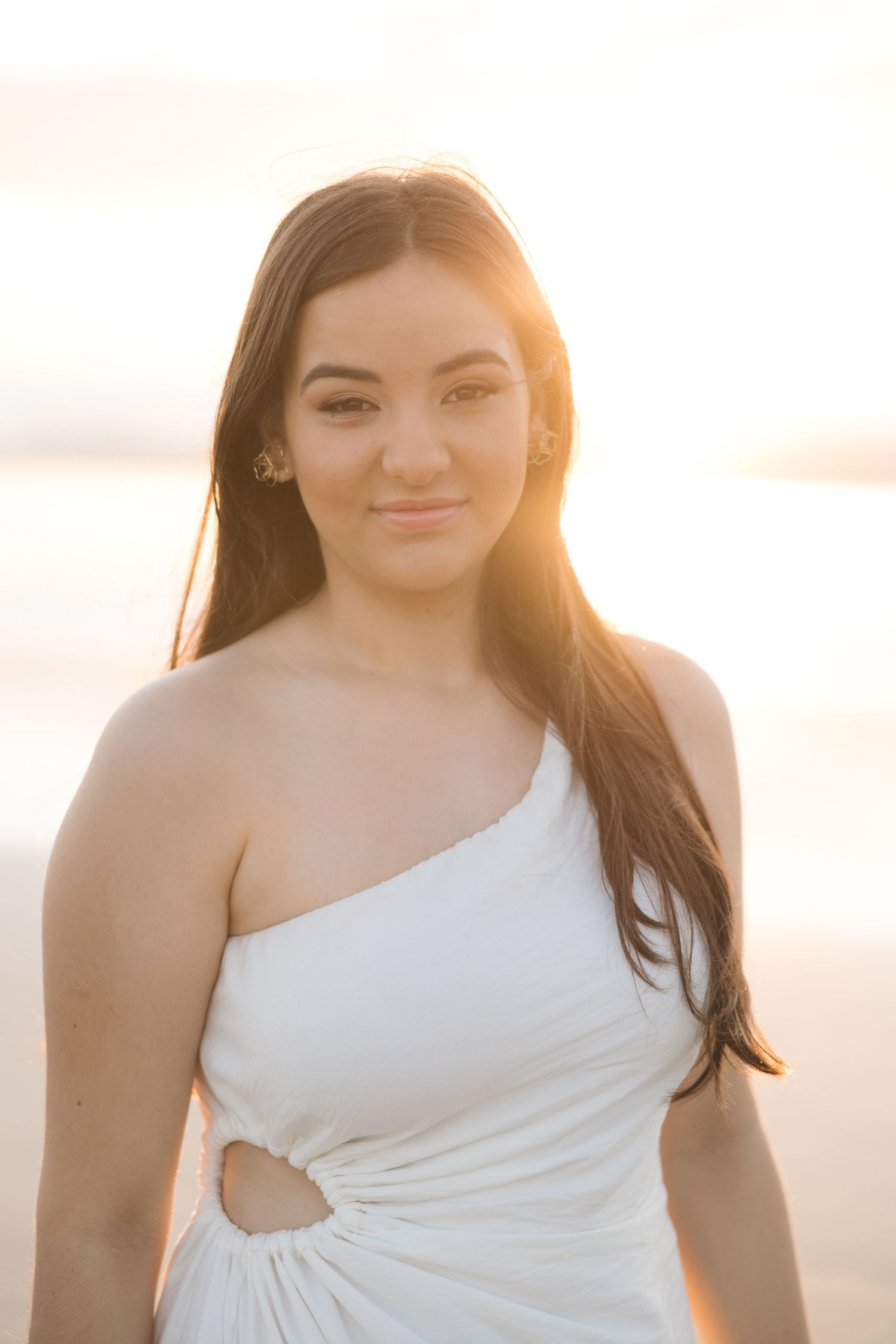 A one-shoulder white dress with cutout detail photographed at sunset with golden light.