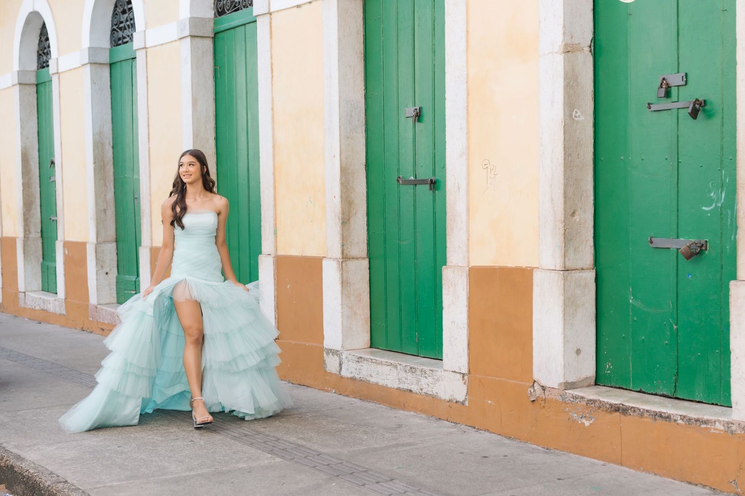 Flowy turquoise gown against a colorful colonial street with green doors and peach-colored walls in Mexico.