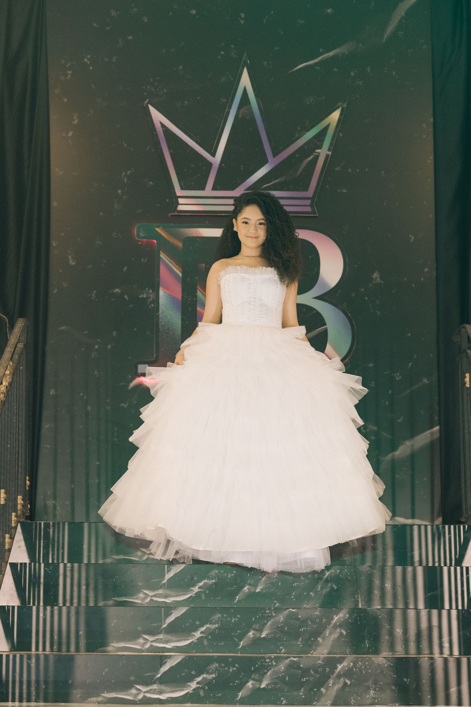 A white ballgown photographed against a dark backdrop with holographic crown design elements.