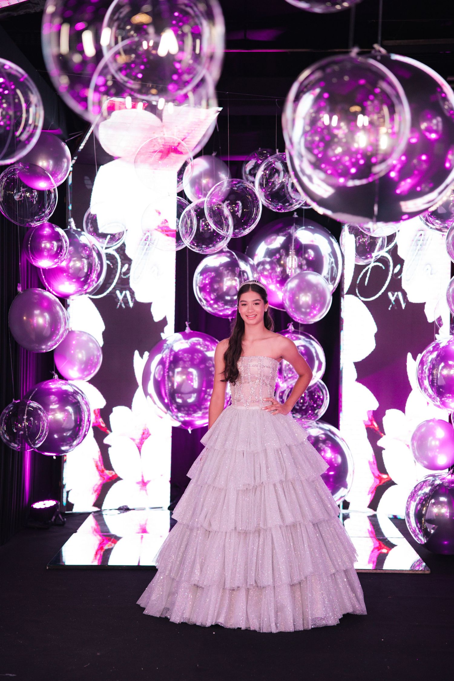Glamorous ballgown photographed against purple balloon and LED wall installation at formal event.