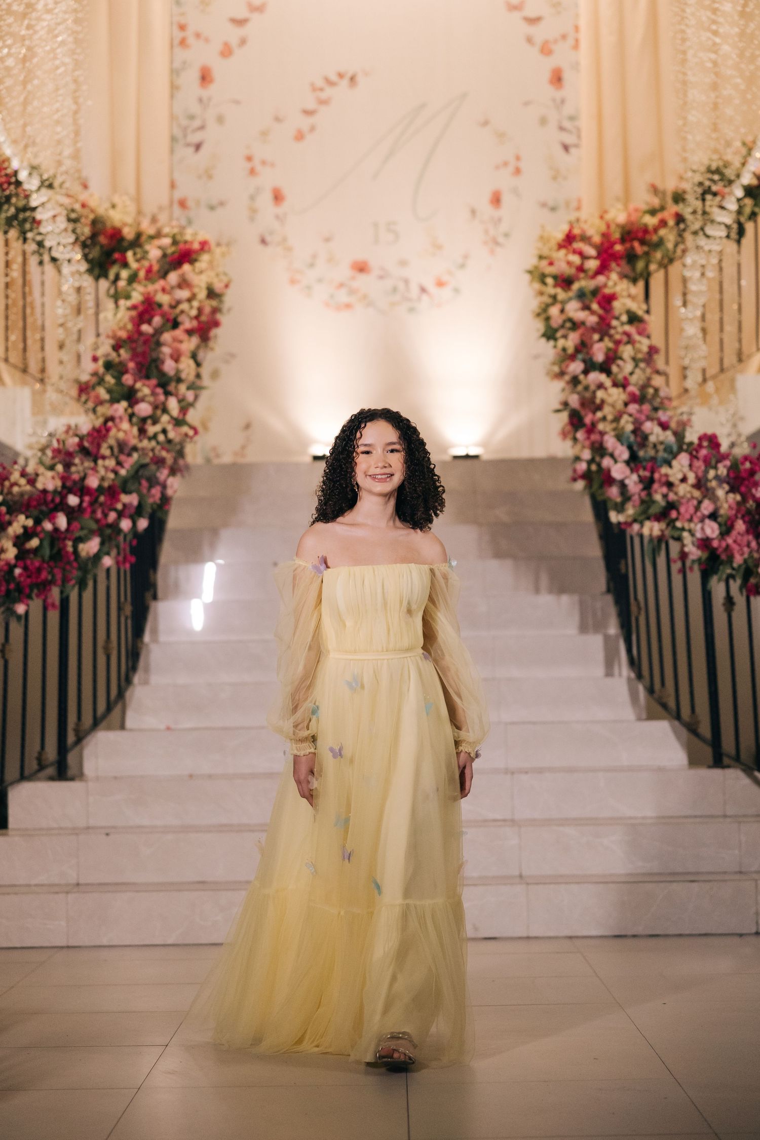 Long yellow tulle dress with off-shoulder design photographed on decorated marble staircase.