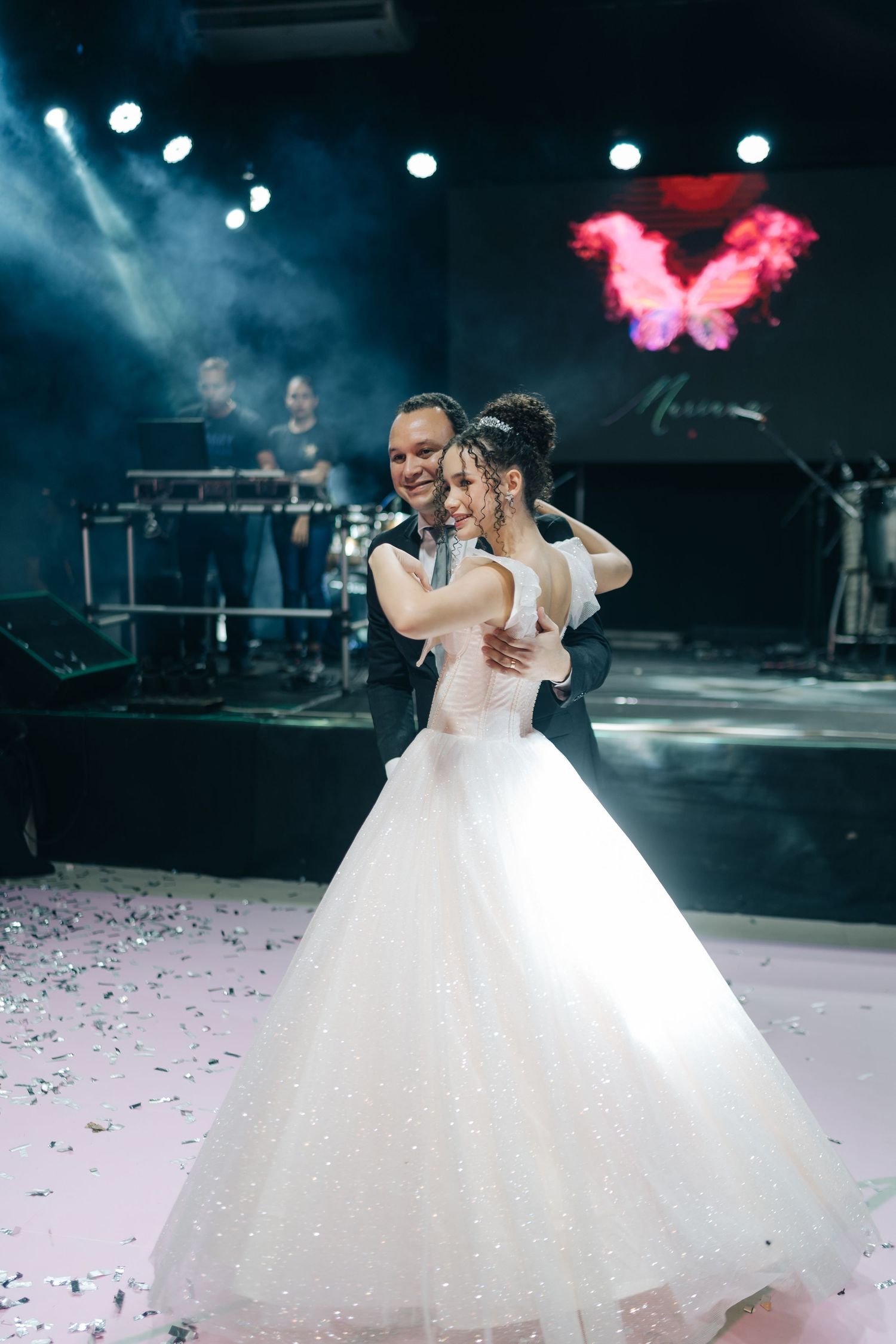 A couple shares their first dance on a misty stage with blue lighting and confetti.