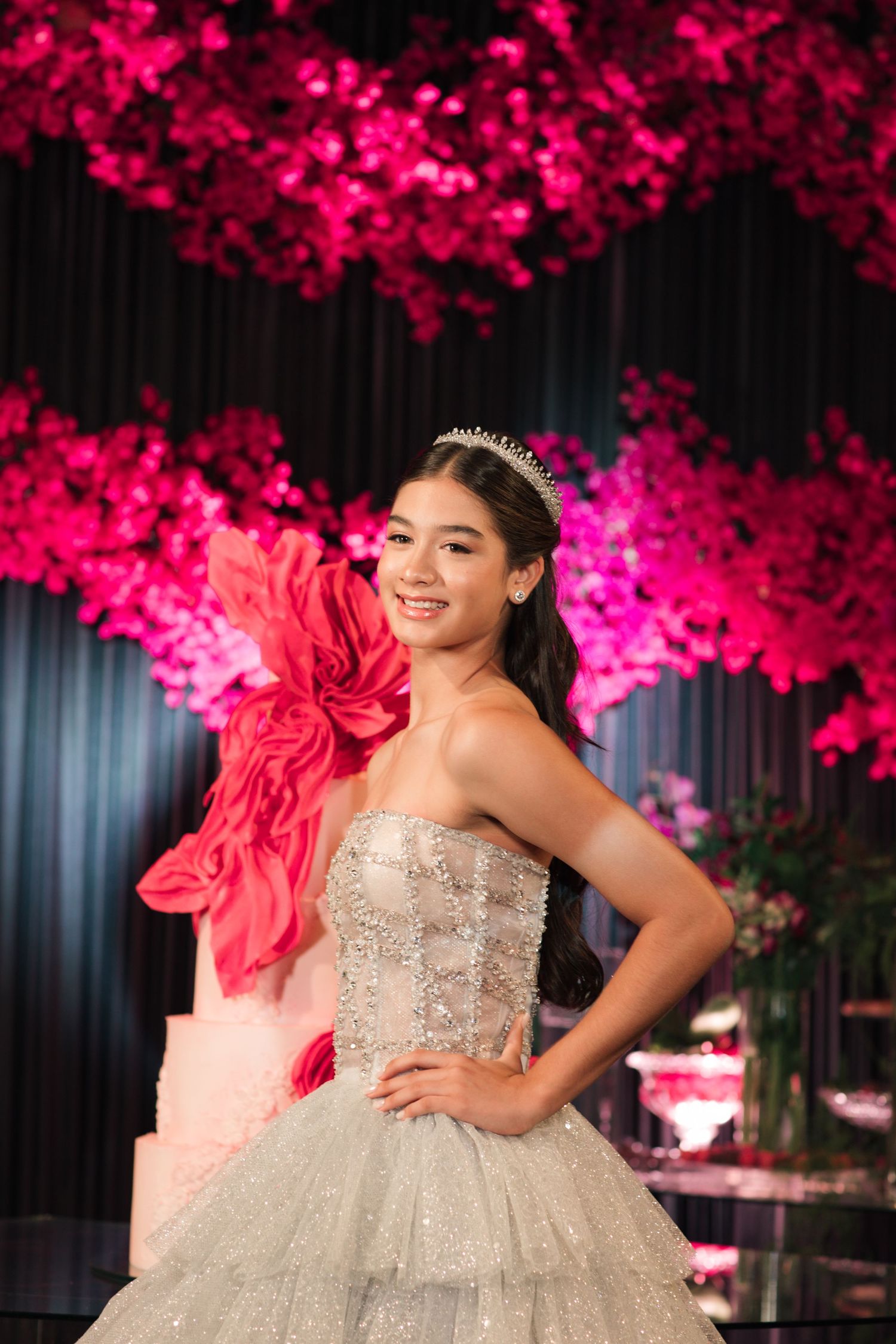 A quinceañera celebration with a stunning silver ball gown under vibrant pink floral decorations.