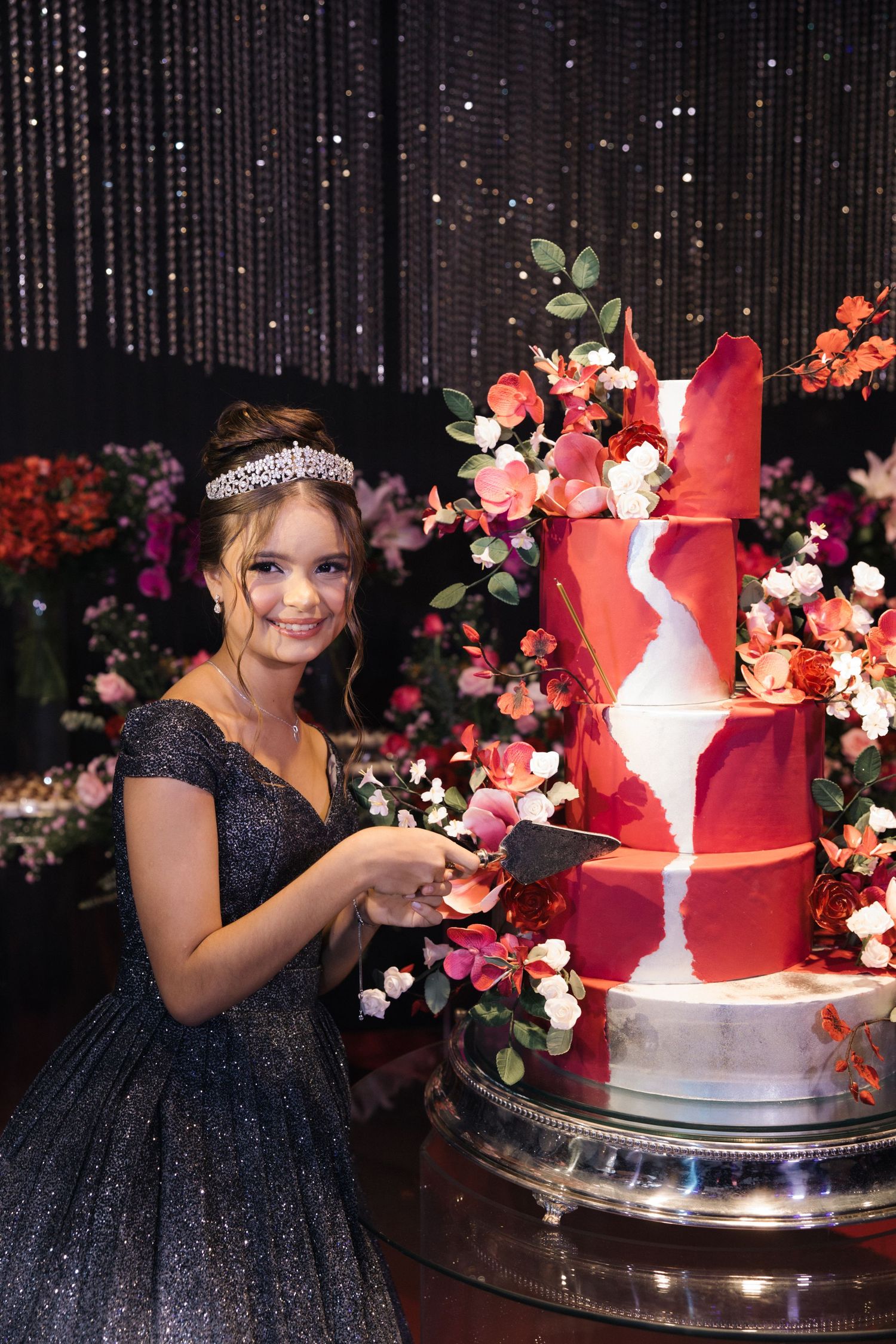 A sparkling black ball gown next to an elegant red and white wedding cake with floral decorations.