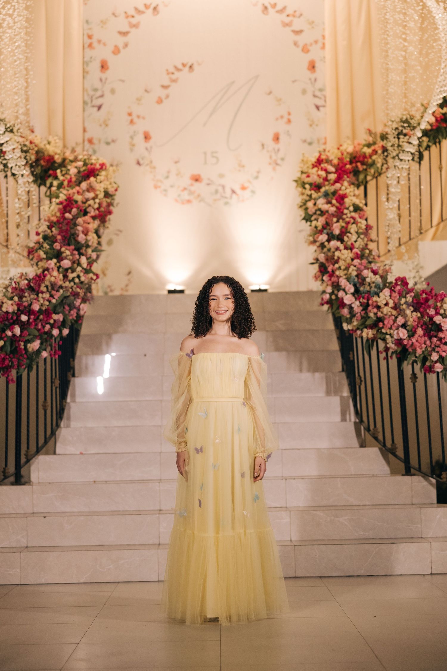 Yellow tulle evening gown photographed on grand staircase decorated with pink floral arrangements.