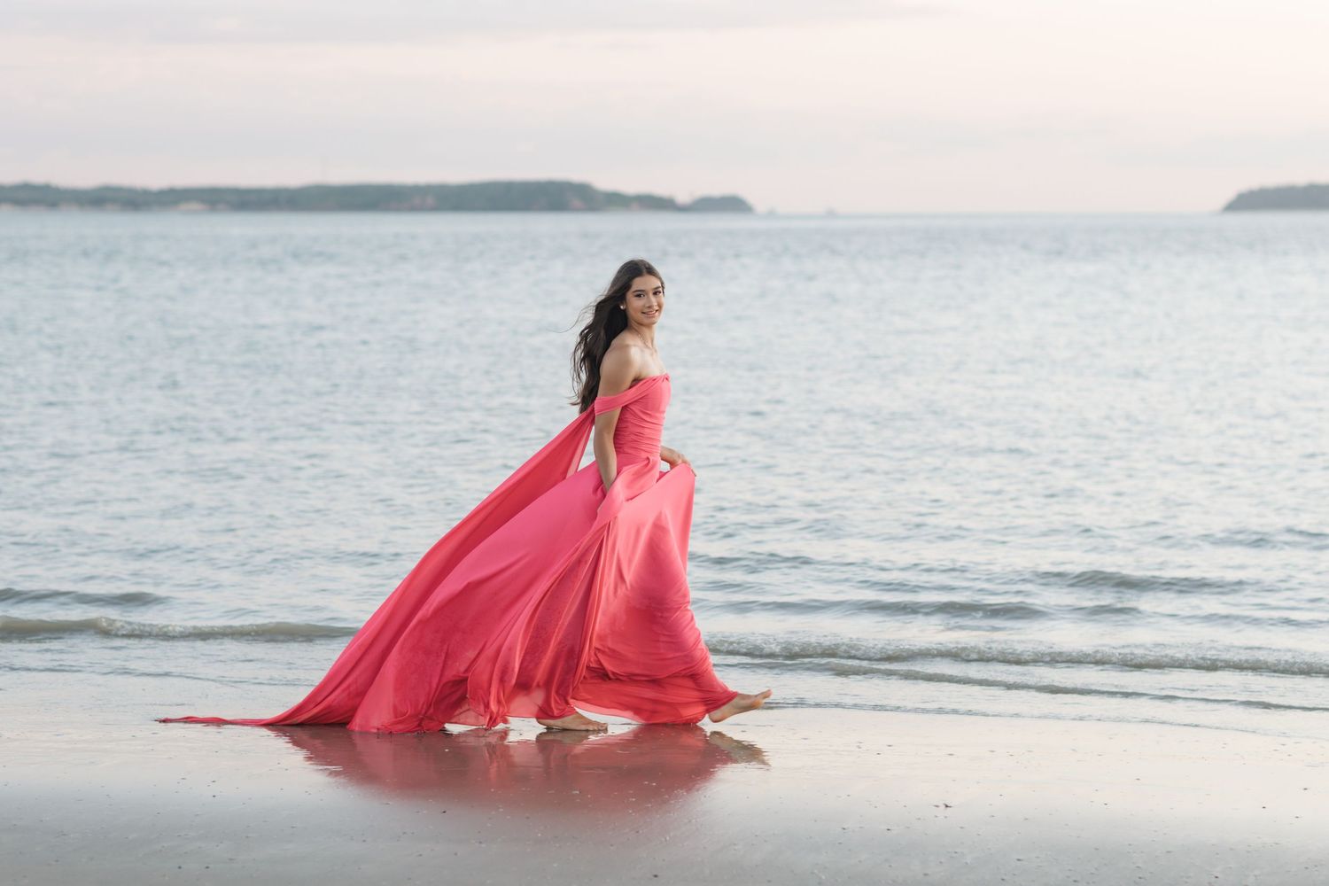Coral evening gown flowing gracefully along the shoreline at dusk.