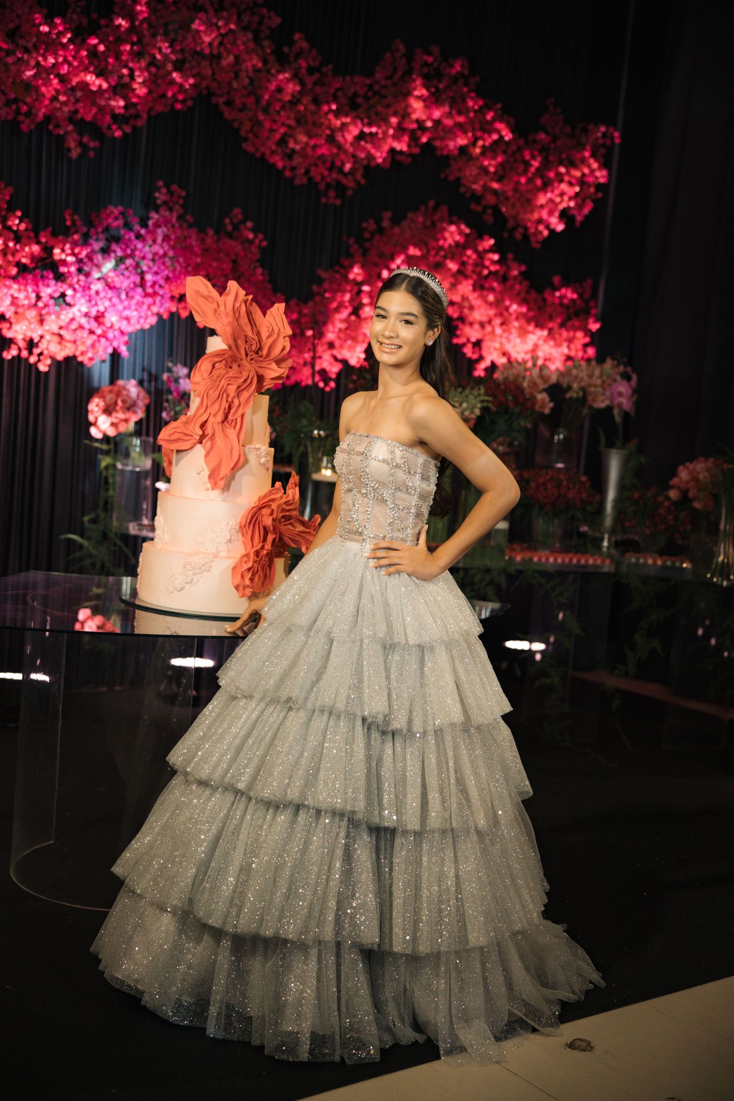 Stunning silver tiered ball gown displayed against pink cherry blossom decorations and a decorative cake at formal event.