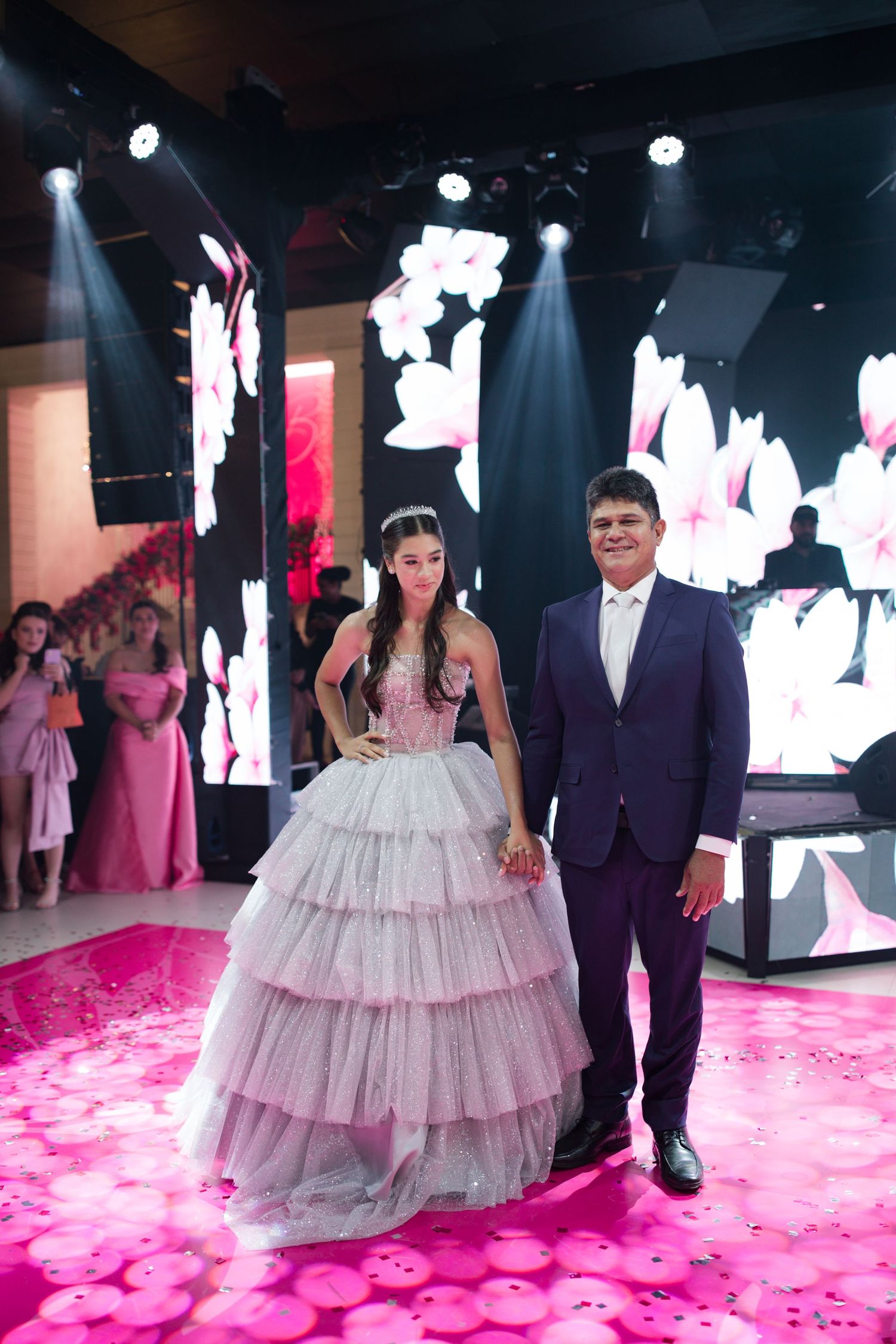A formal couple poses on a pink-lit dance floor with digital displays in an elegant venue setting.