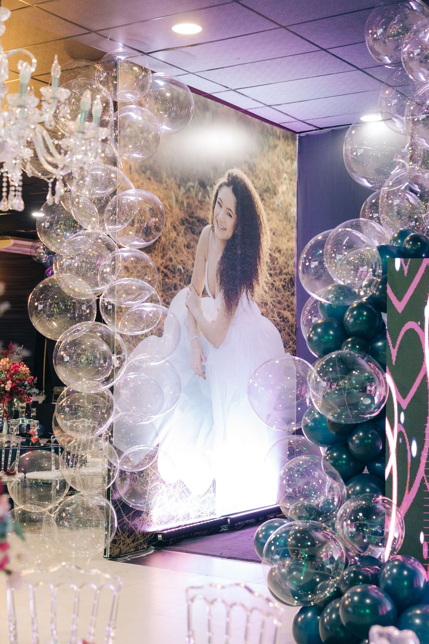 A dreamy event setup with clear balloons and teal accents framing a backlit display.