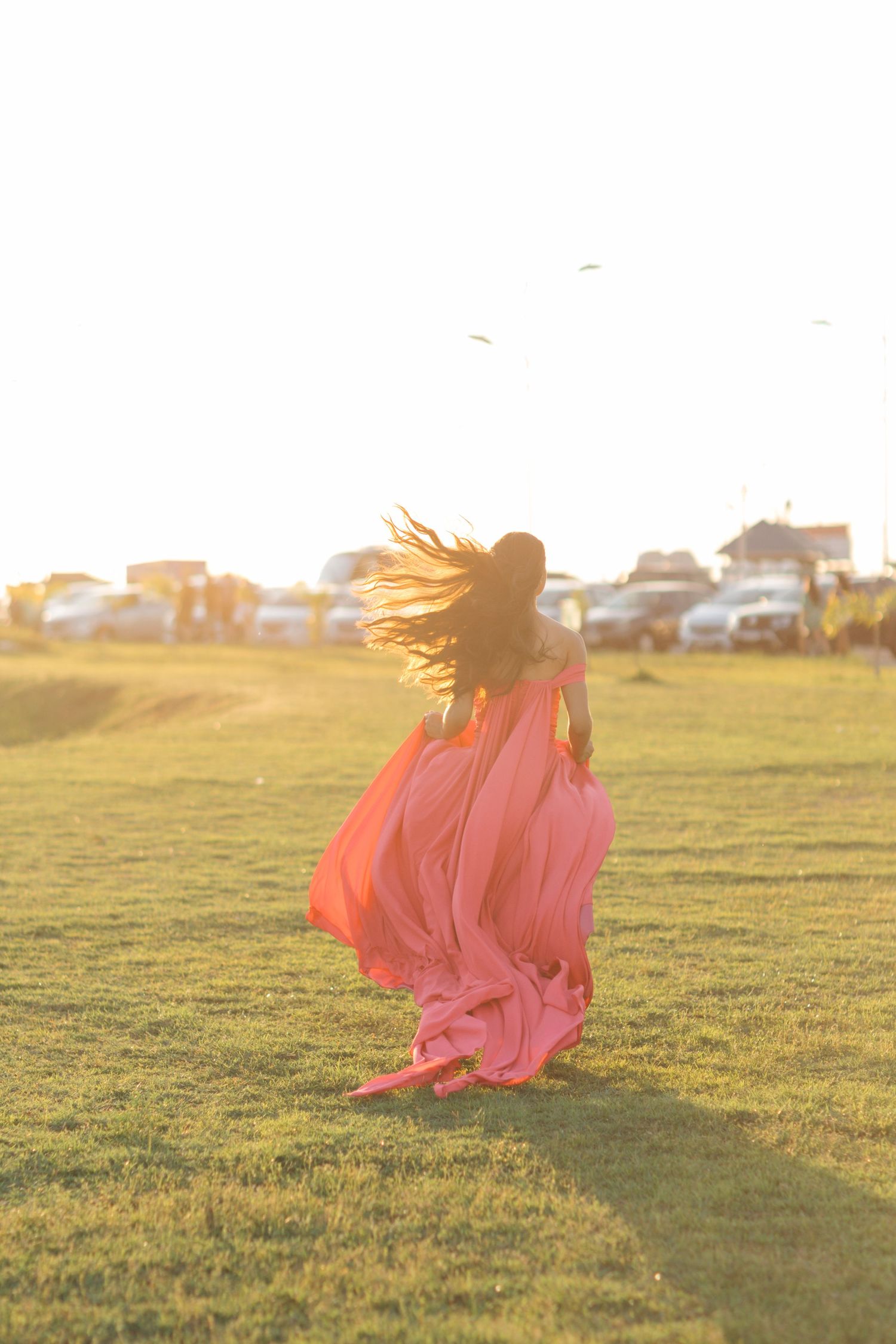 Silhouette of a flowing coral dress against golden sunlight in a grassy field at sunset.