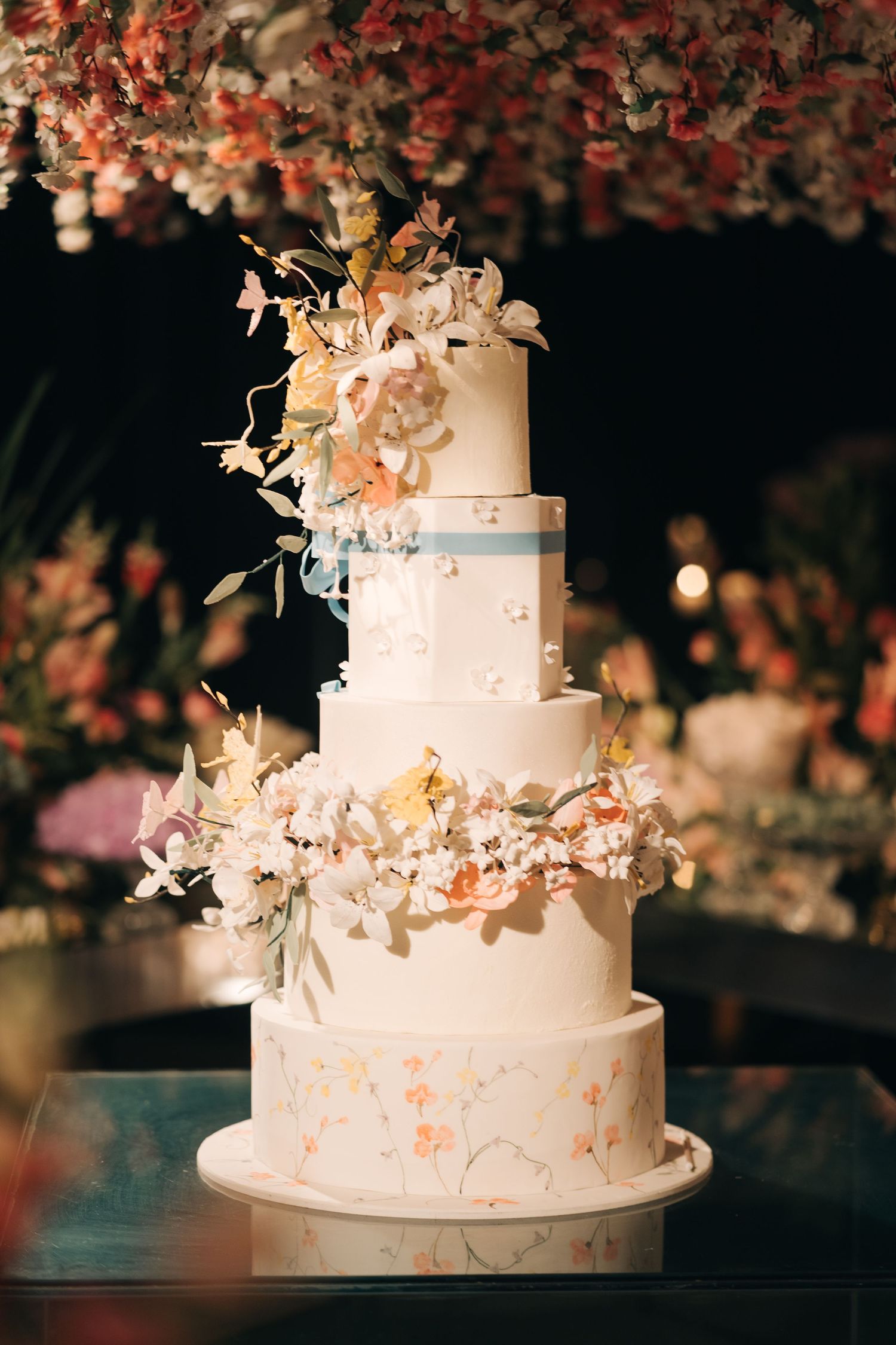 Elegant four-tier white wedding cake decorated with delicate floral details and marbled accents.