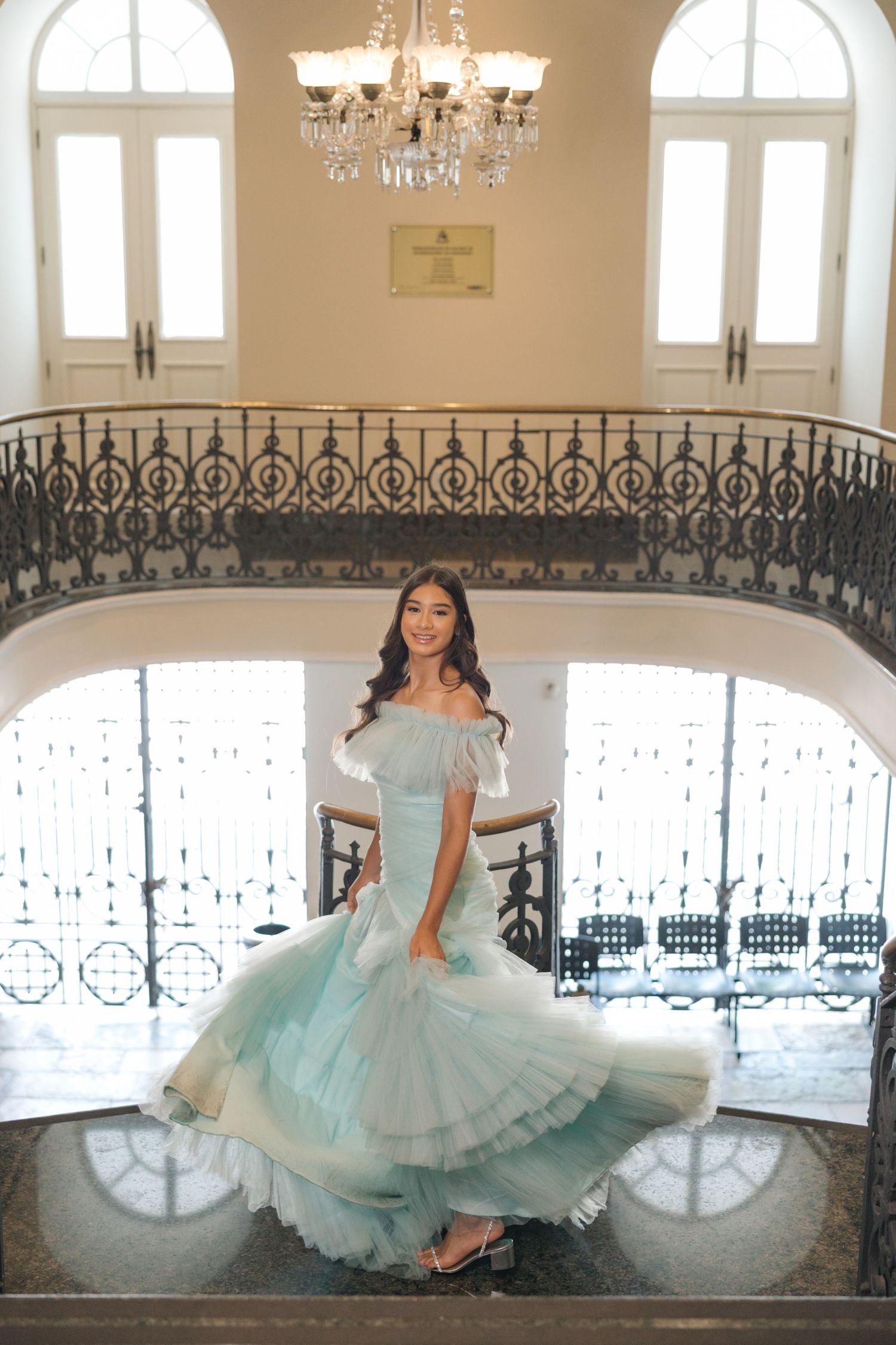 Ethereal mint green gown photographed on an elegant staircase with ornate iron railings and crystal chandelier.