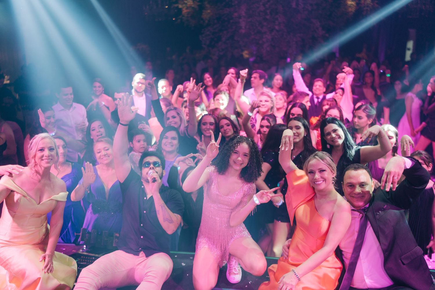 Crowded dance floor with party-goers dancing under pink and blue stage lighting.