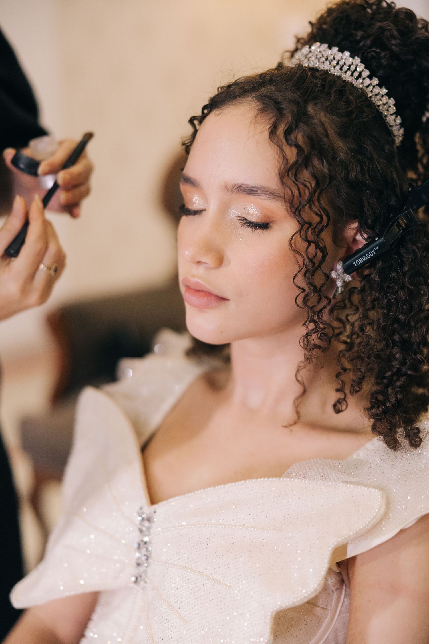 Close-up shot of bridal makeup application showing intricate curls and crystal tiara.