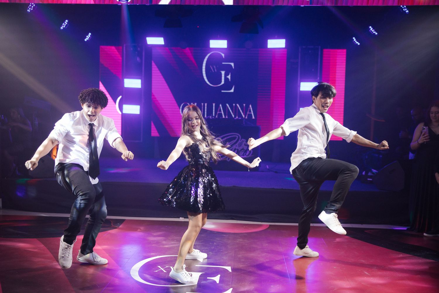 Dancers perform energetic choreography on a purple-lit nightclub stage with illuminated Luanna signage in the background.