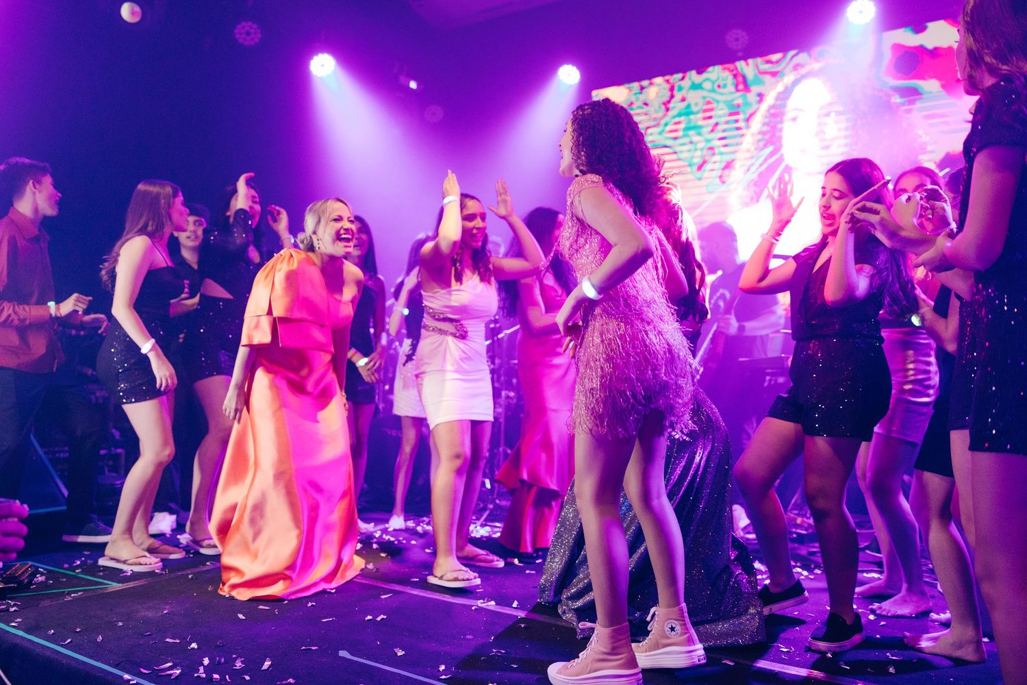 Energetic dance party scene with purple lighting and festive crowd on dance floor.