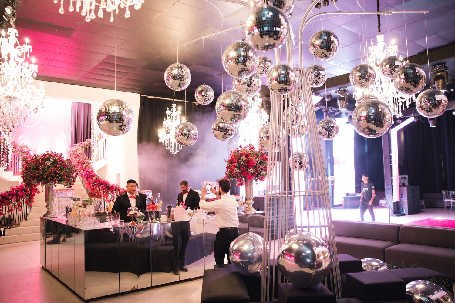Luxurious event space decorated with mirror balls, chandeliers, and pink floral arrangements.