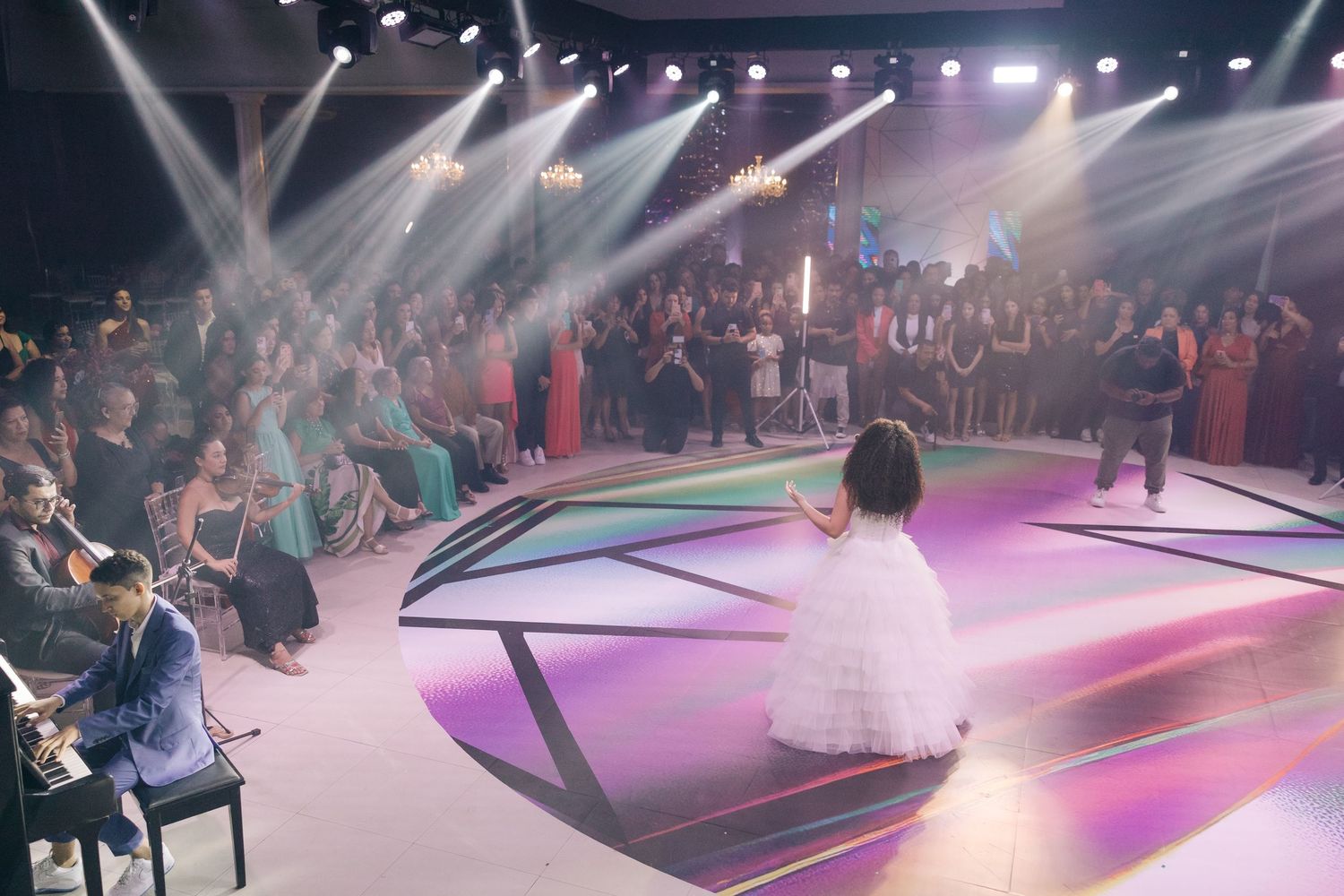A grand celebration with spotlights illuminating a white dress on a modern geometric stage design.