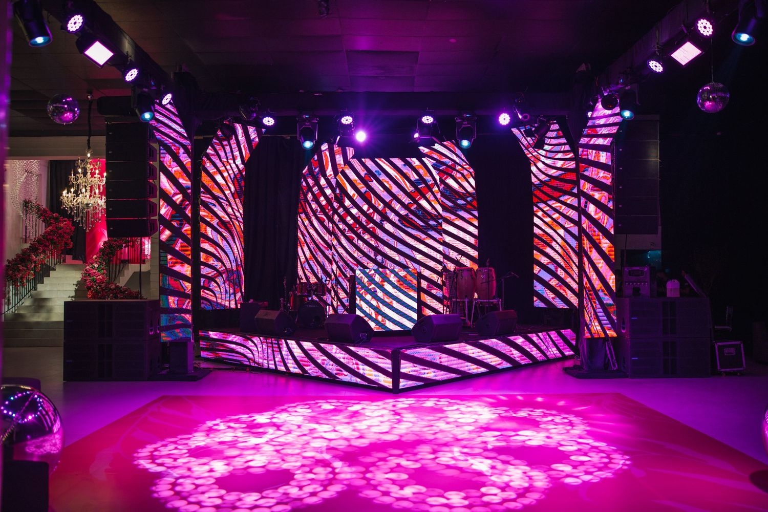 A modern event space with geometric LED displays and pink floor lighting creates a dynamic party atmosphere.