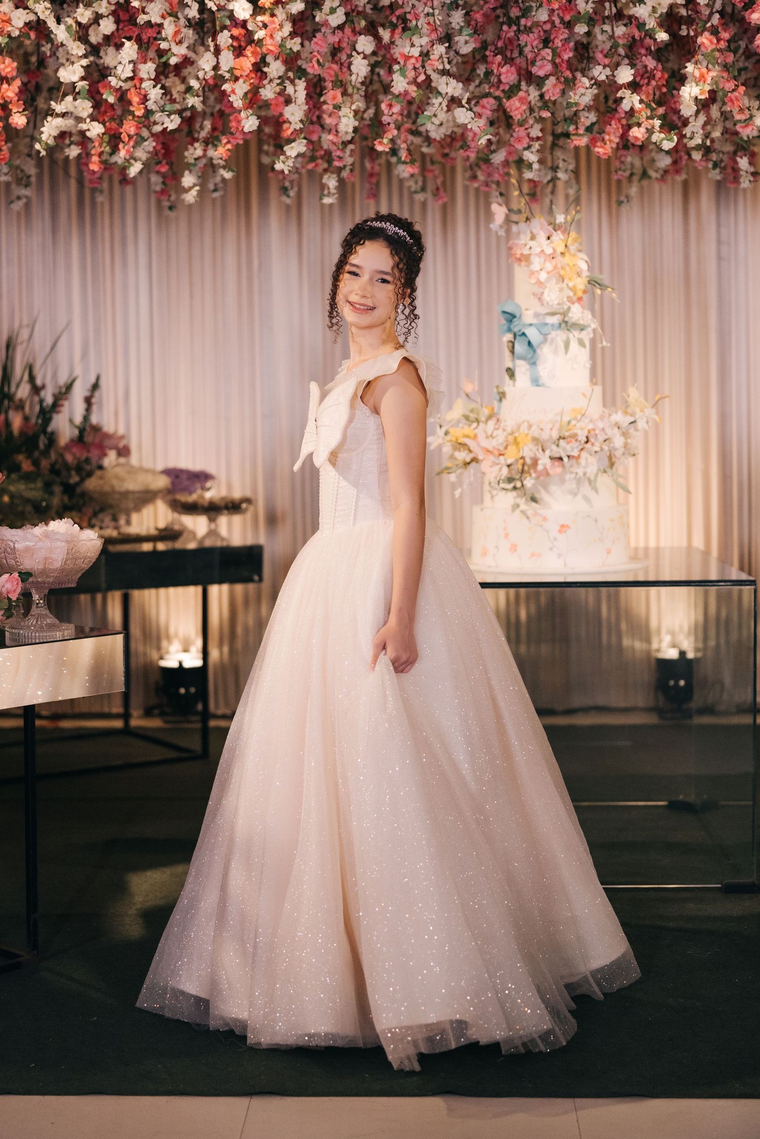 A wedding celebration features an elegant tiered cake and cascading pink florals above a beautiful bridal display.