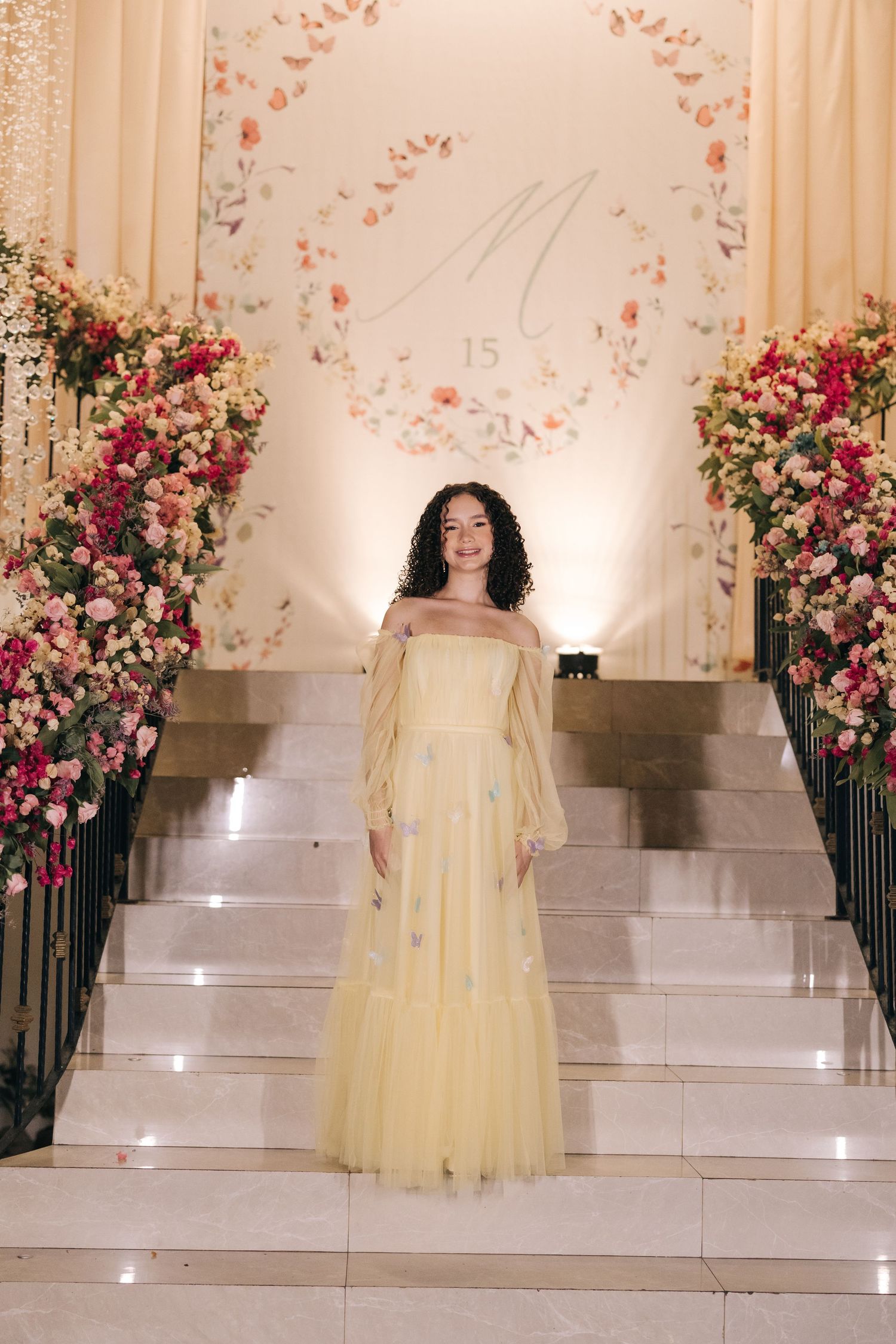 Elegant pale yellow tulle gown showcased on marble stairs with romantic floral decorations.