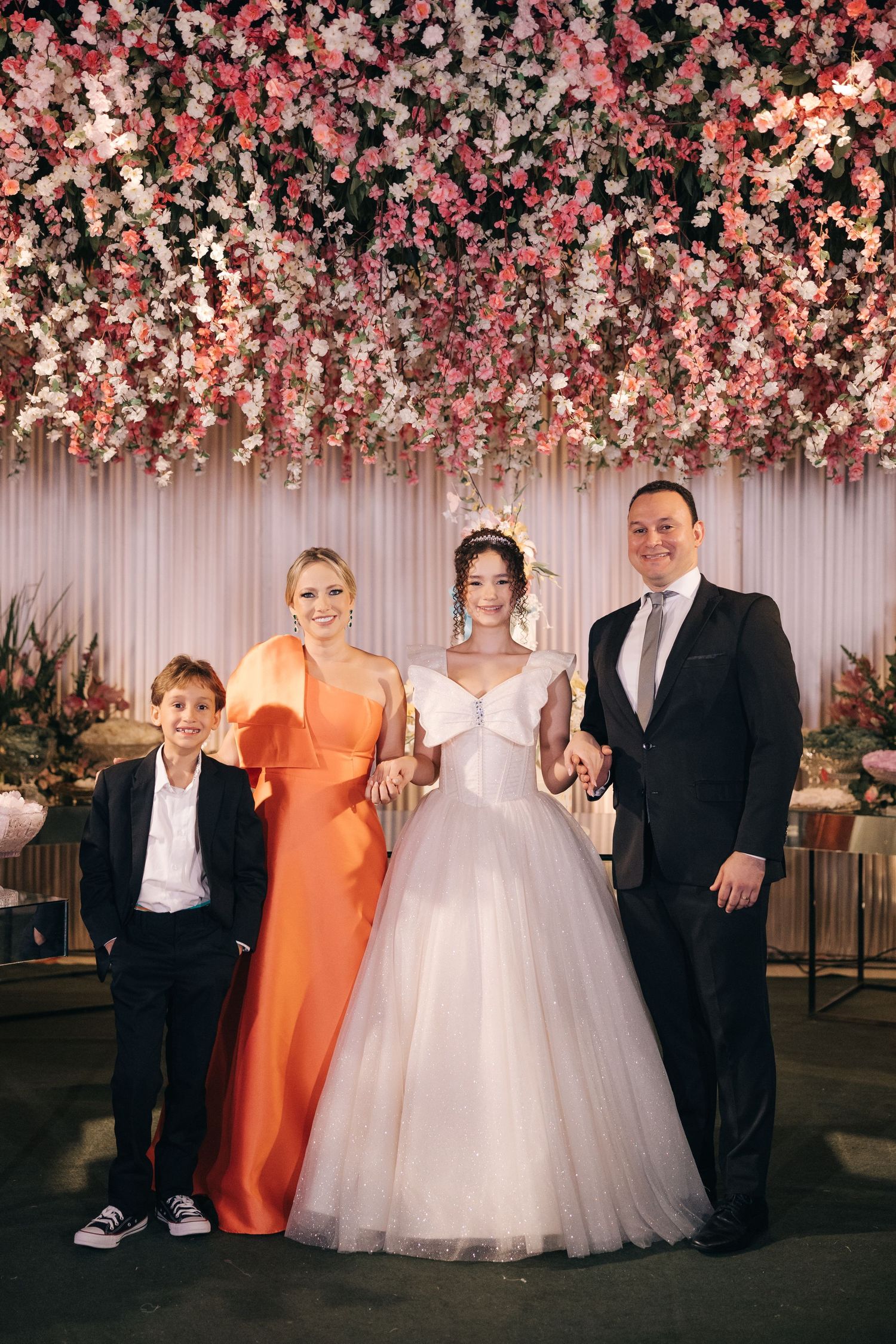 Wedding party poses together under a stunning pink floral ceiling installation at an elegant reception.