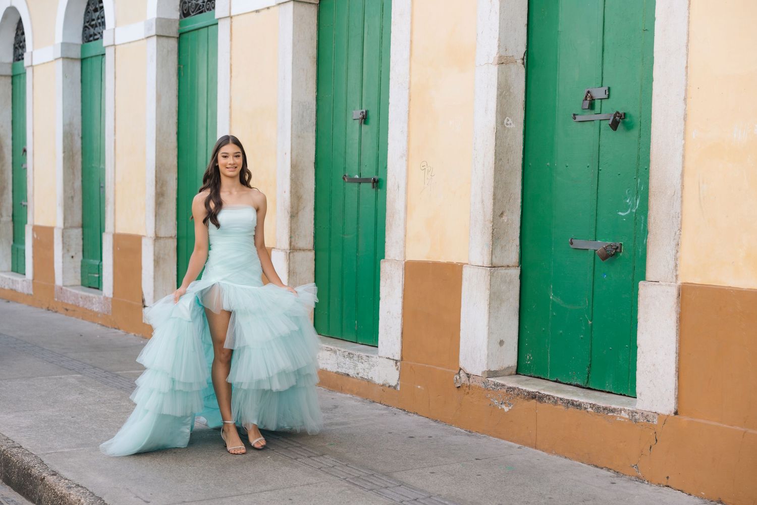 A light blue tulle gown flows gracefully against vibrant green colonial doors and cream colored walls on a historic street.