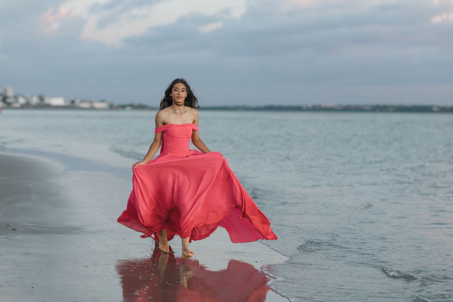 A coral pink flowing dress catches the ocean breeze during a beachside photoshoot.