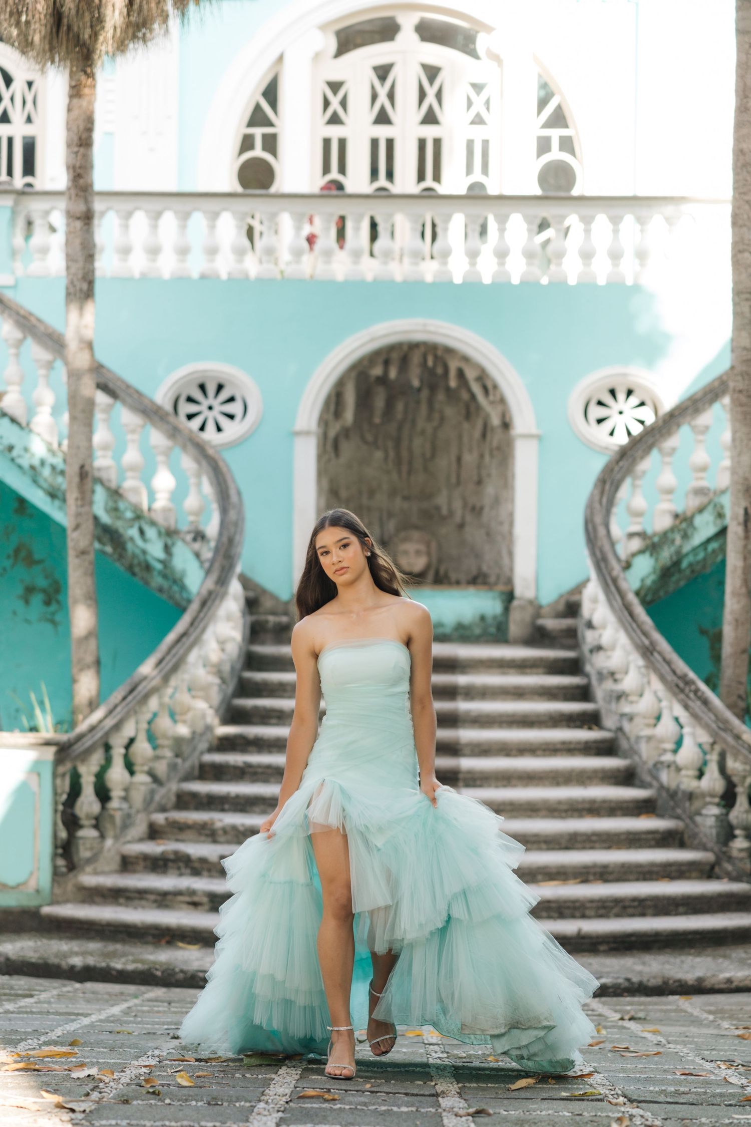 Flowing seafoam green dress with tulle layers photographed against turquoise architectural details and grand staircase.