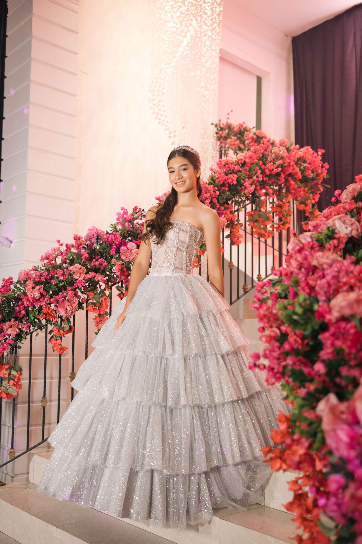 Elegant silver ballgown photographed against white staircase decorated with vibrant pink flowers.