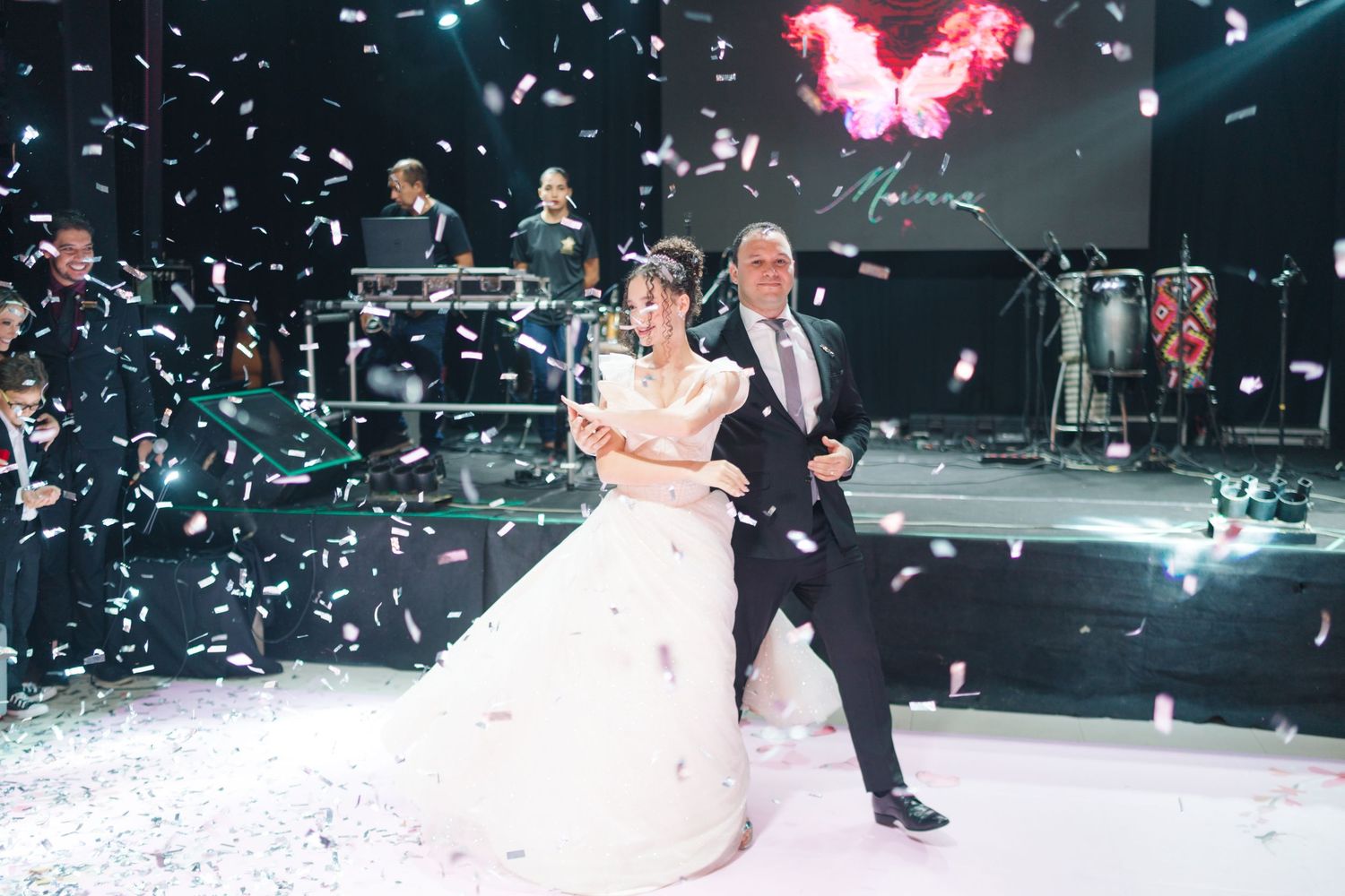 Wedding couple dancing amid falling confetti on illuminated dance floor with pink lighting effects.