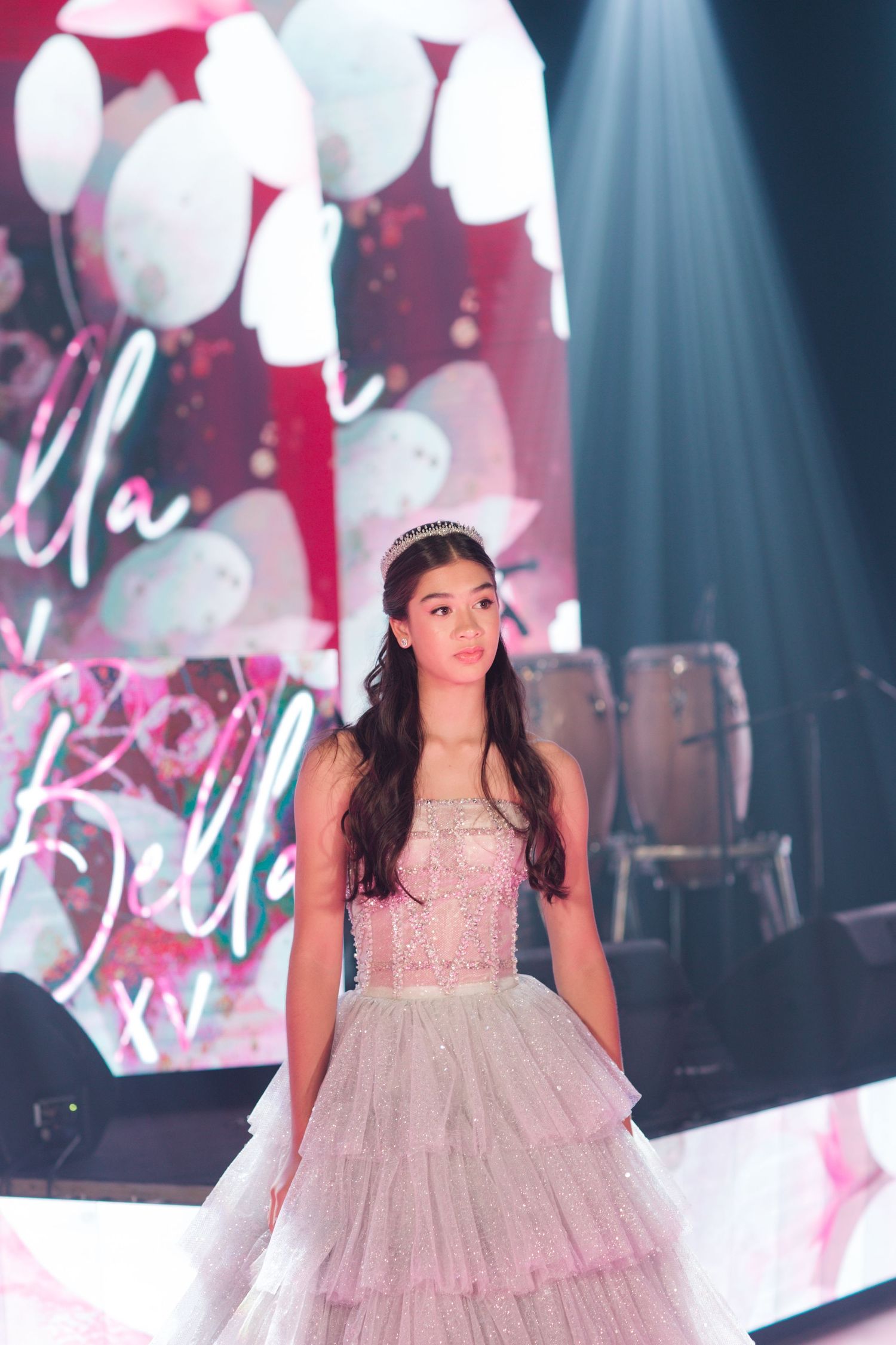 Ethereal princess ballgown captured under dramatic spotlight with pink backdrop and white balloons.