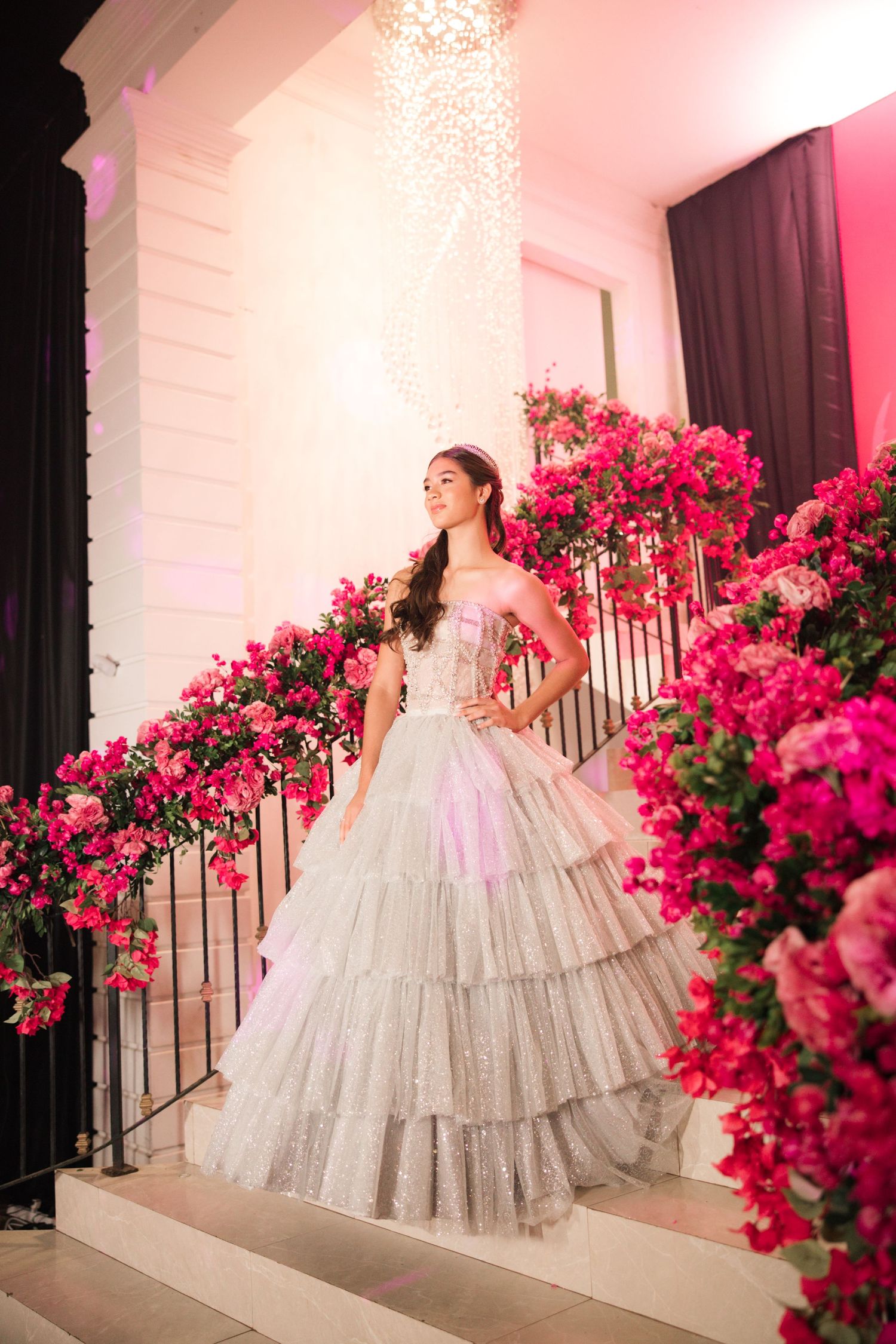 Dreamy portrait of silver ballgown against white architecture and pink floral decorations.